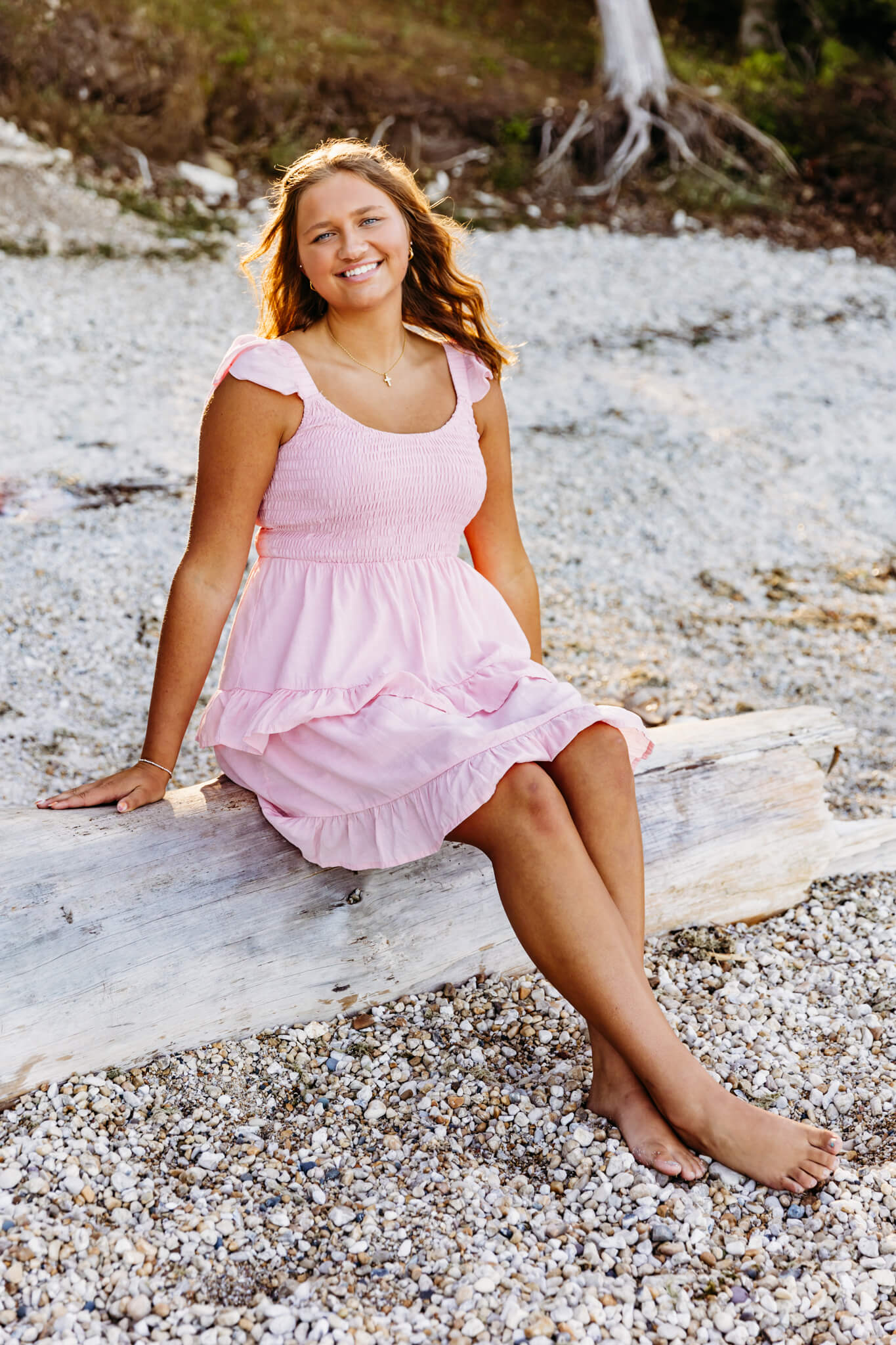 Ashwaubenon High School student in a pink dress sitting on a piece of driftwood in Door County 