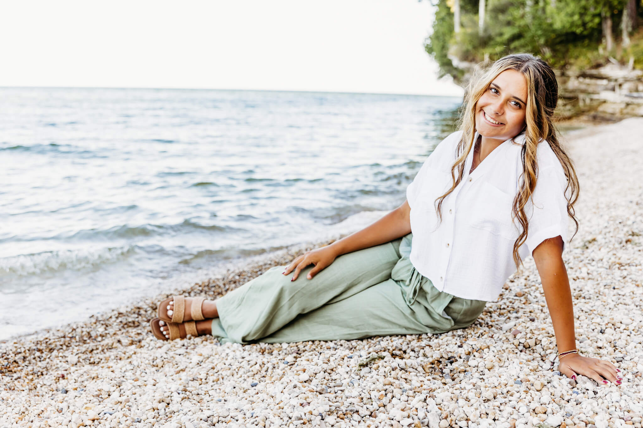 Teenage girl in a white top and green pants sitting on a beach and smiling