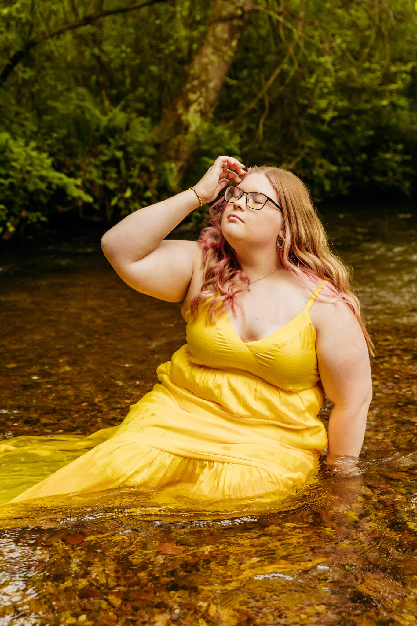 high school girl sitting in a river creek in a yellow dress for senior photos