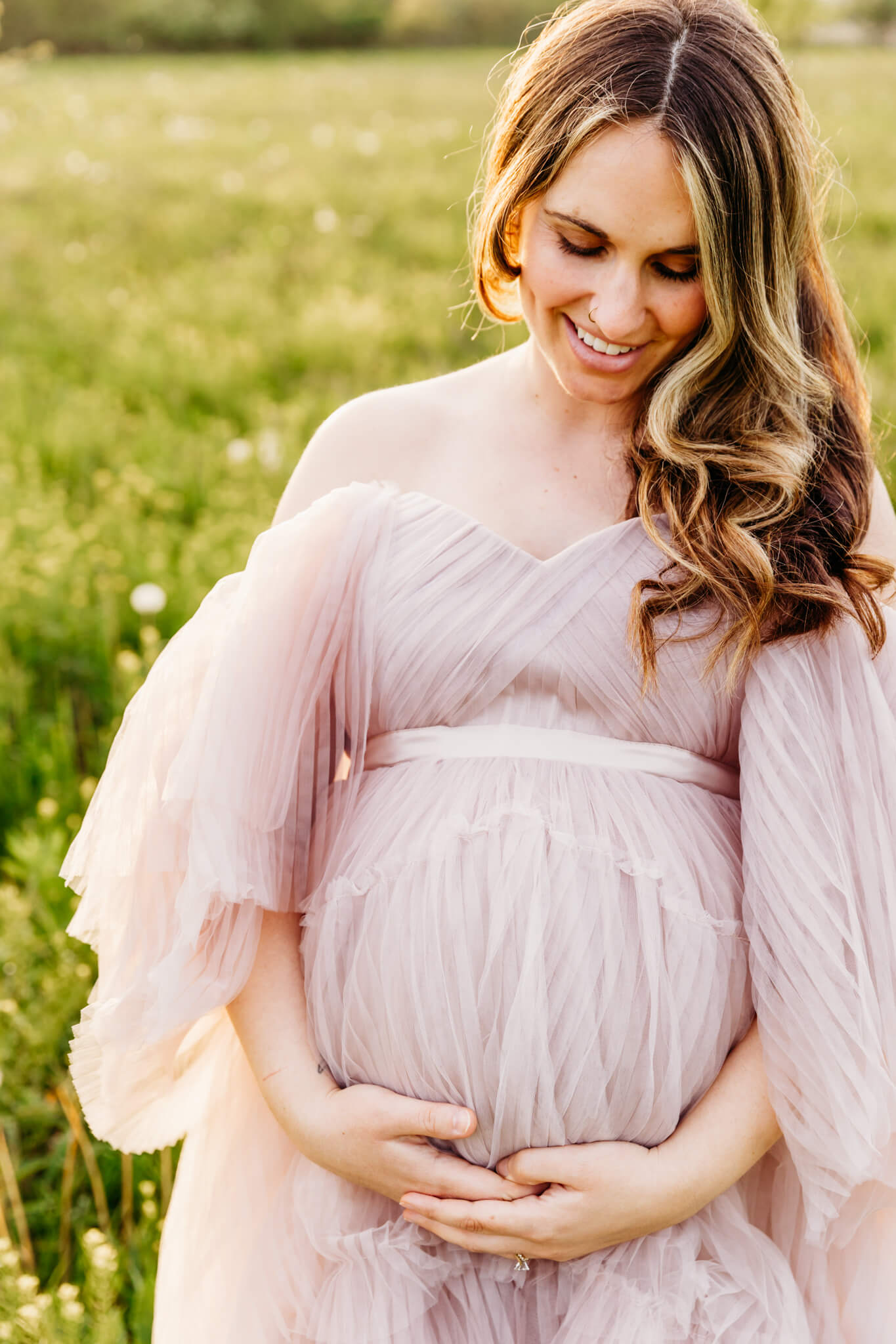 mom to be holds her baby bump and smiles as she looks down in a grassy field near Omro WI