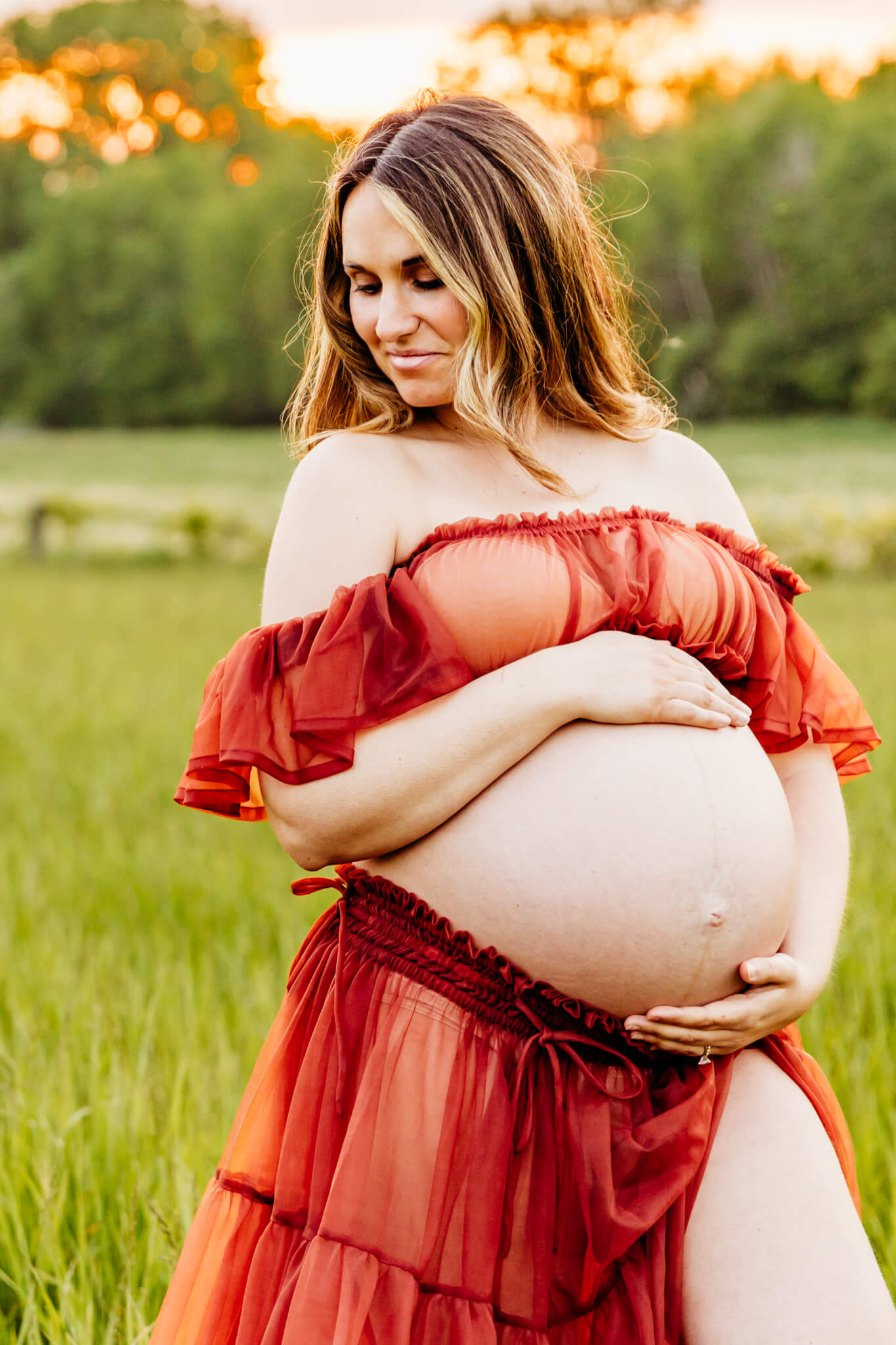 beautiful mom to be in an orange two piece dress holding baby bump as she looks down at shoulder
