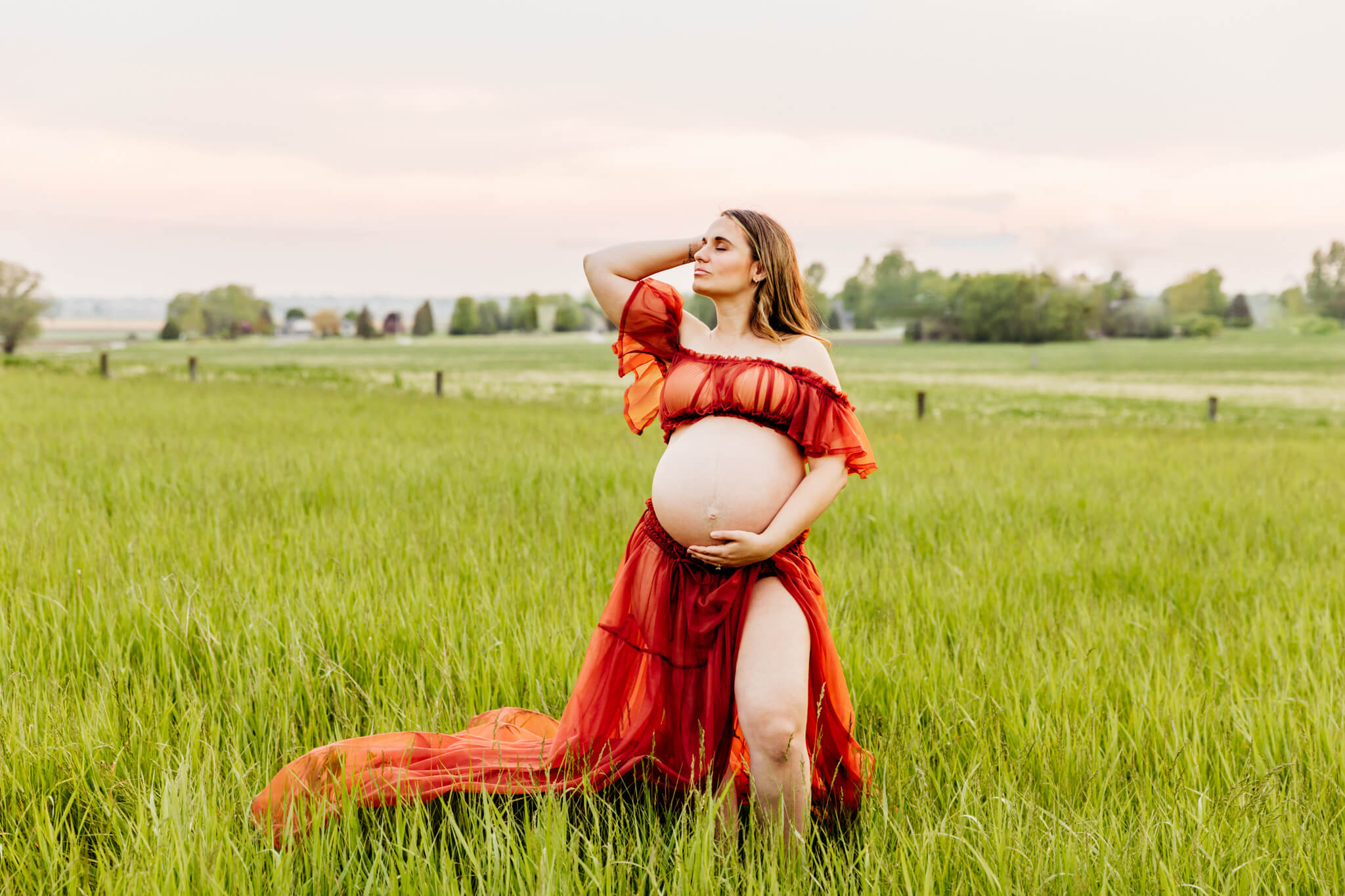 gorgeous expecting mama holding her baby bump and pulling her hair back in a field with a beautiful sunset