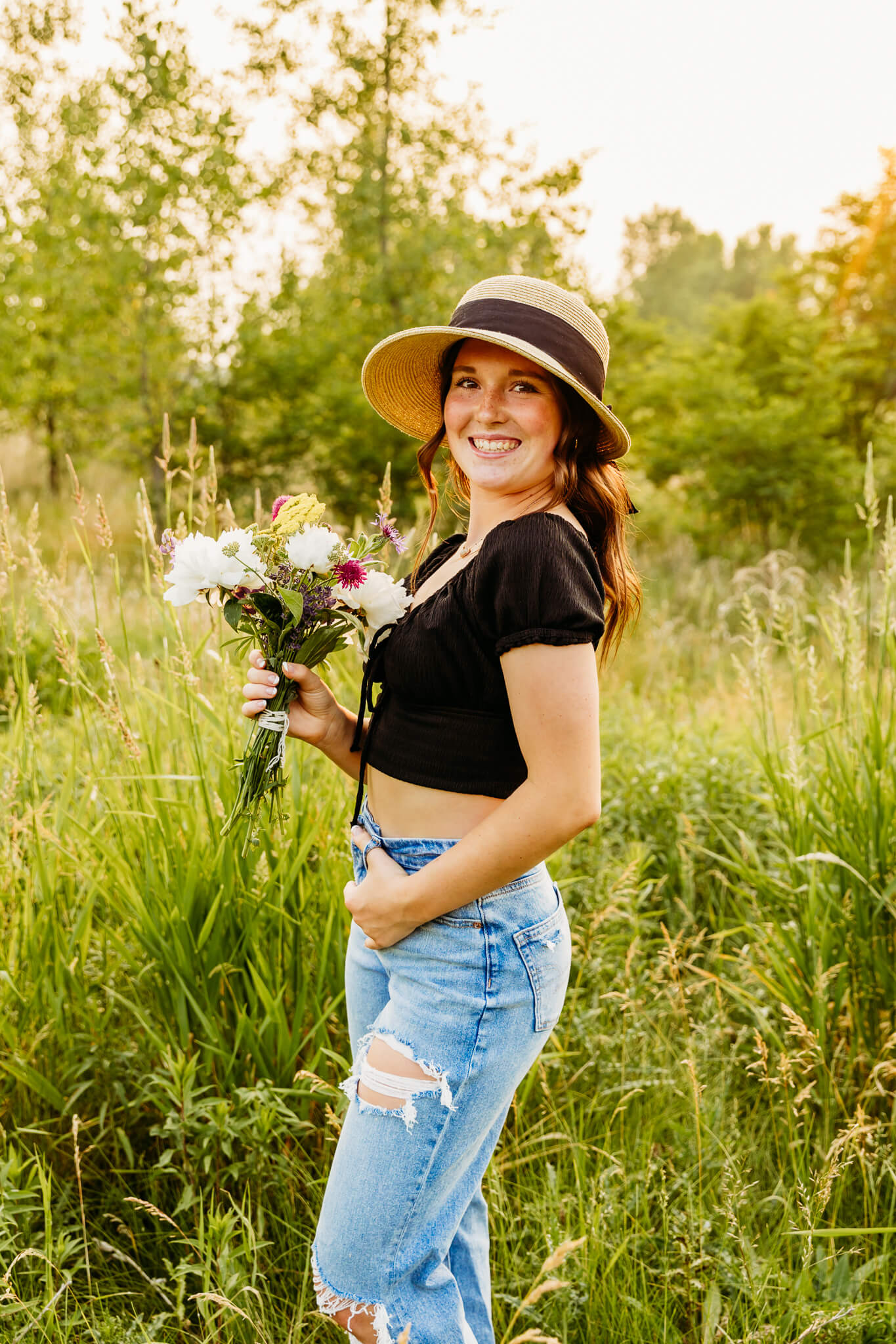 senior girl wearing a hat and holding a bouquet of wildflowers