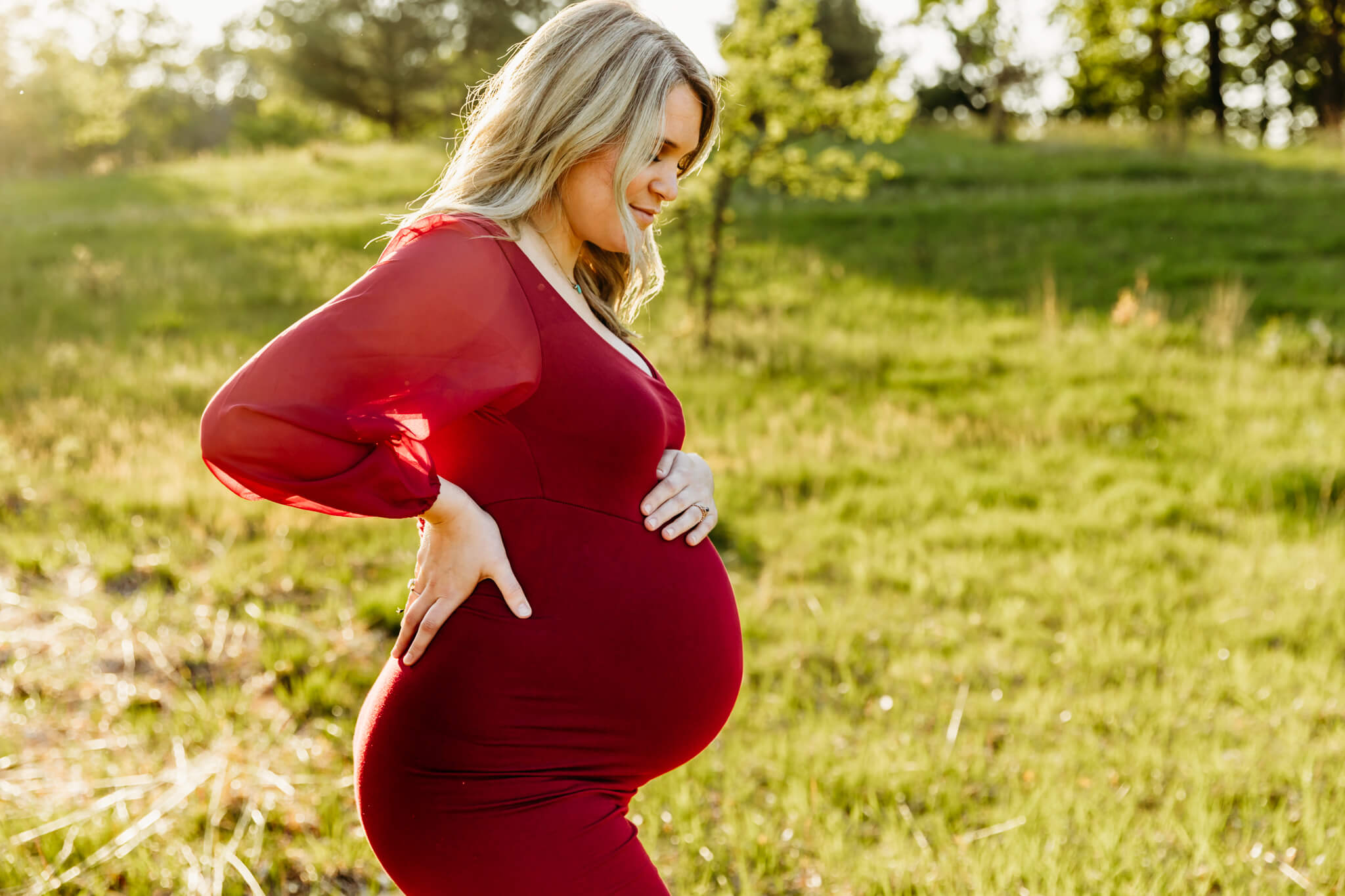gorgeous mom to be gazing down at her baby bump while wearing a fitted red gown