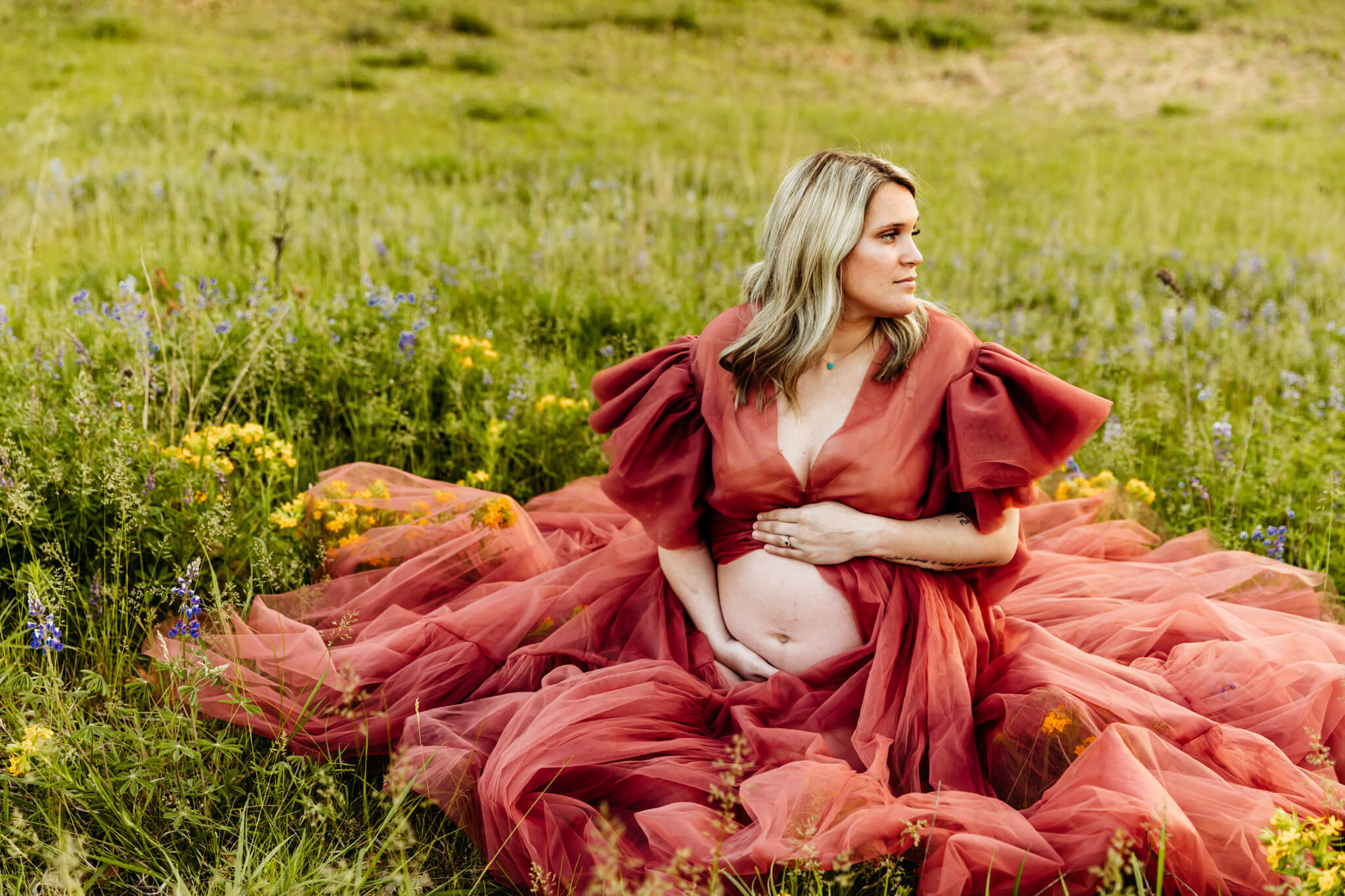 expecting mother holding her baby bump that's peeking through her robe as she looks out into the wildflower field