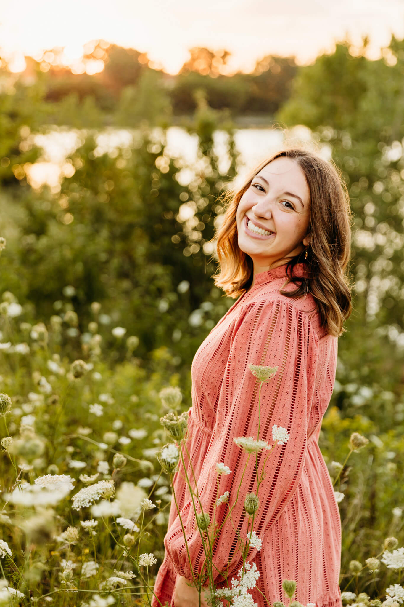 high school senior in a pink dress looking over shoulder in a field of wildflowers