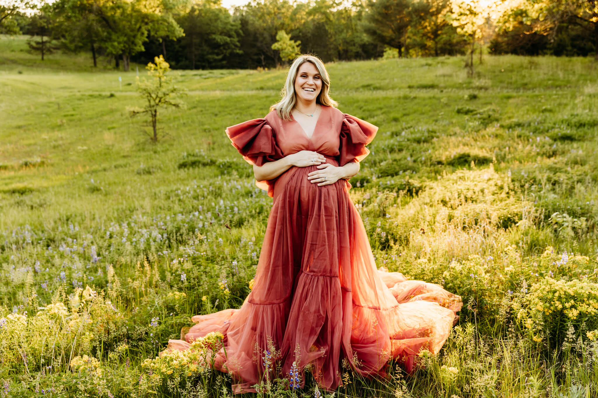 stunning mom to be posing while resting her hands on her baby bump in a spring flower field