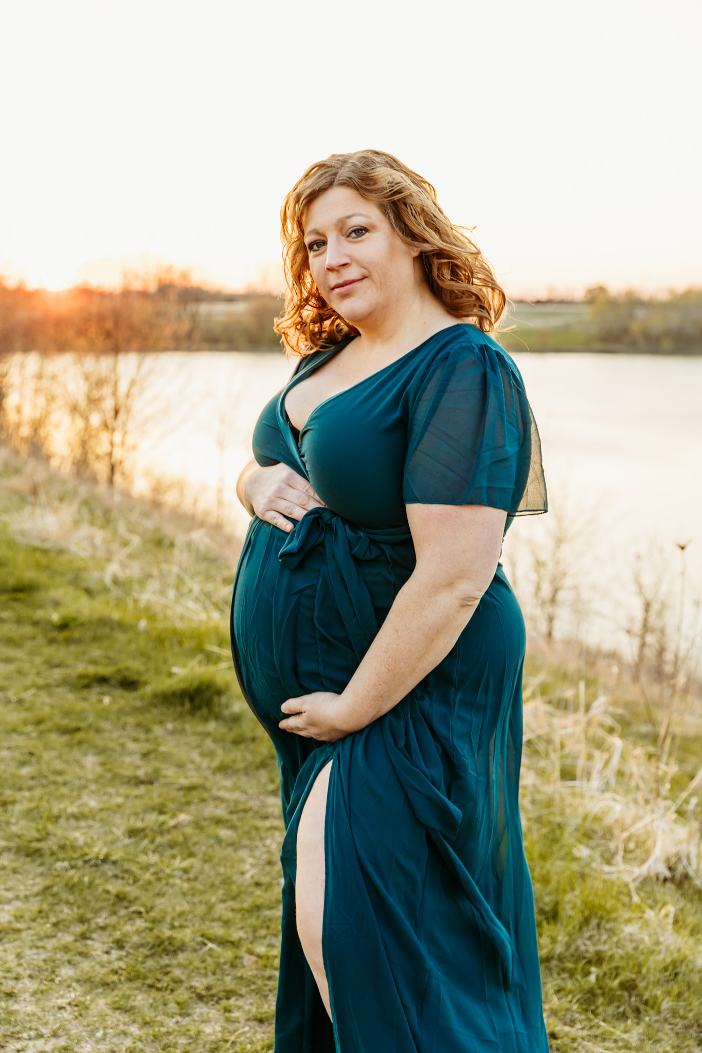 A mom to be in a blue maternity gown stands by a lake holding her bump green bay massage therapy