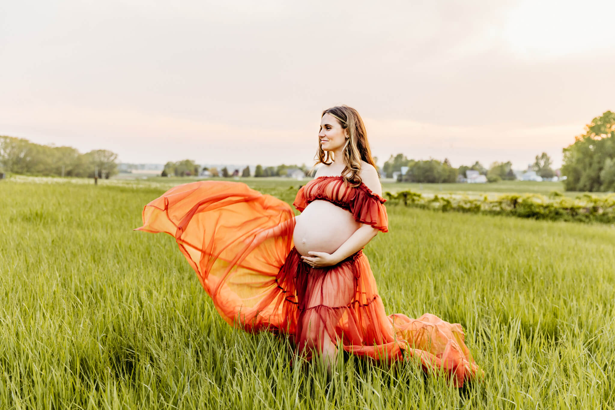mom to be throwing her orange skirt into the wind as the sun sets behind her in a beautiful field