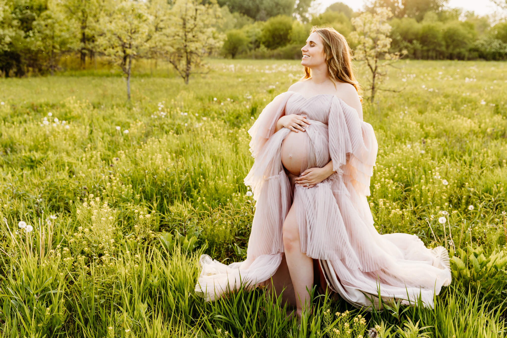 stunning mom to be stands in the middle of a flower field and holds her baby bump as she closes her eyes