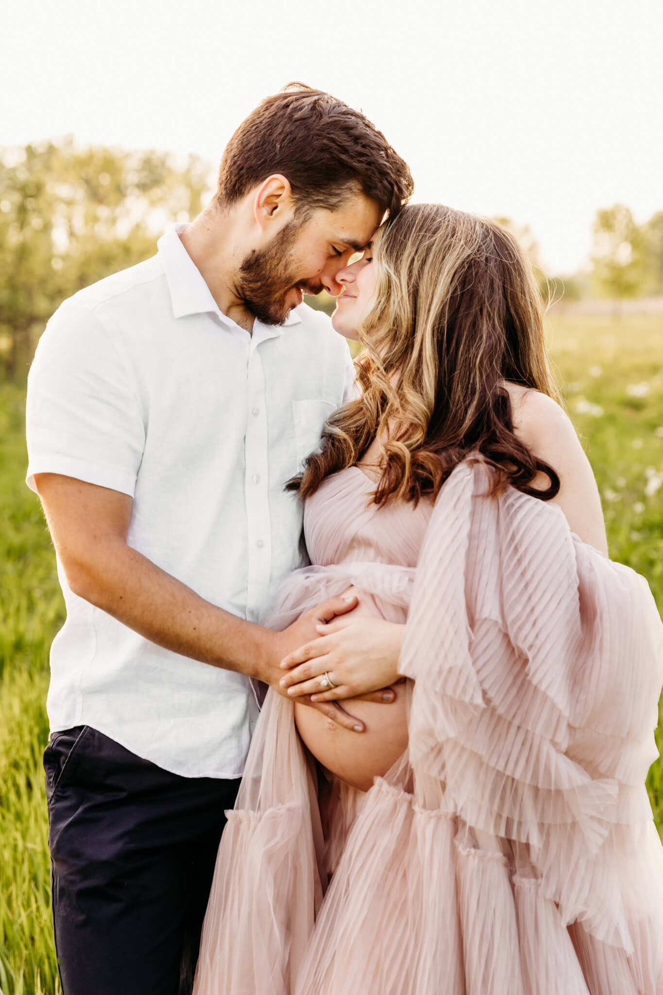 gorgeous couple holding each other and embracing their soon to be baby as they touch foreheads in a park near Oshkosh