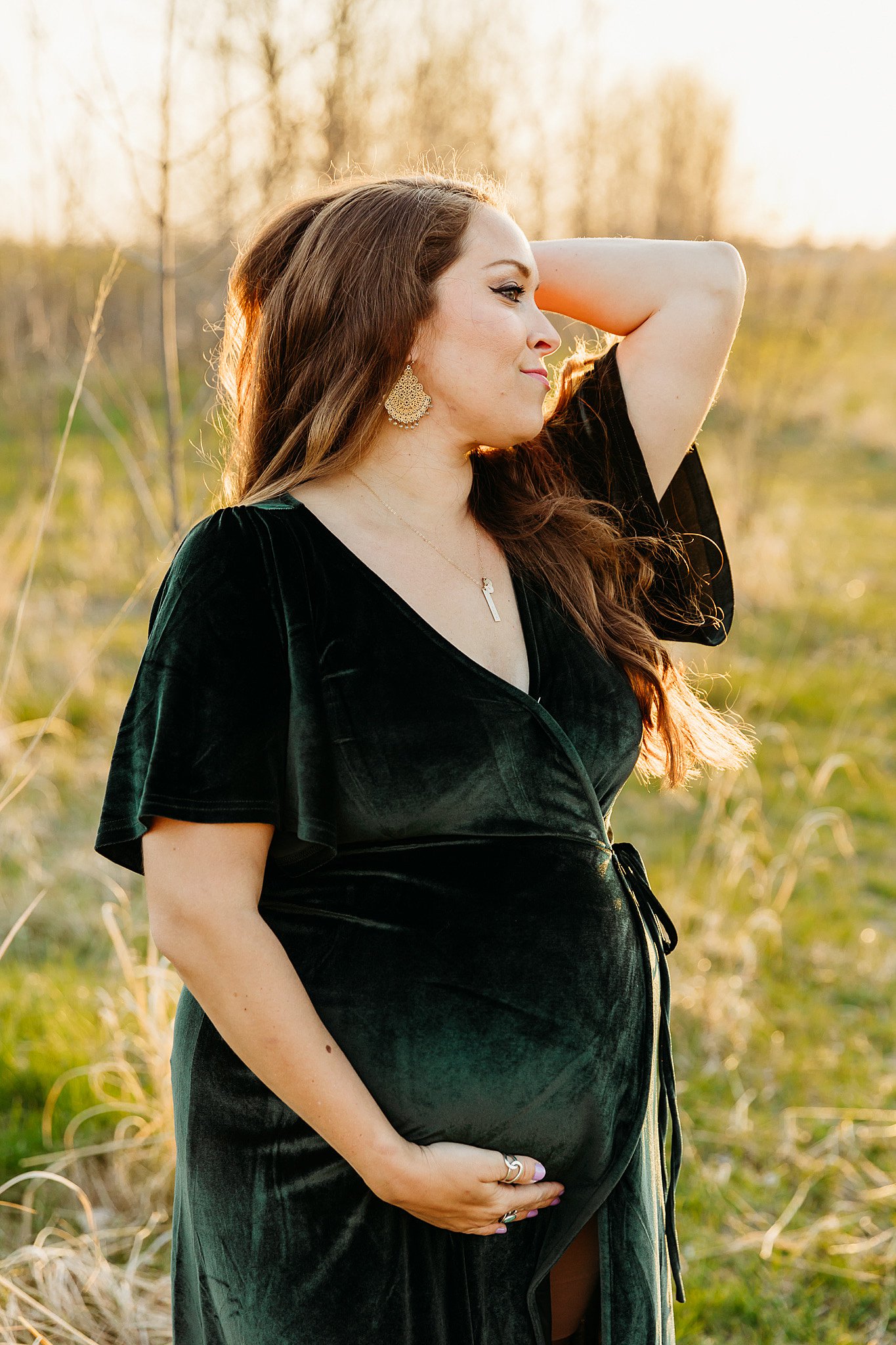 A mother to be in a green velvet dress stands in a grassy field New beginnings pregnancy center