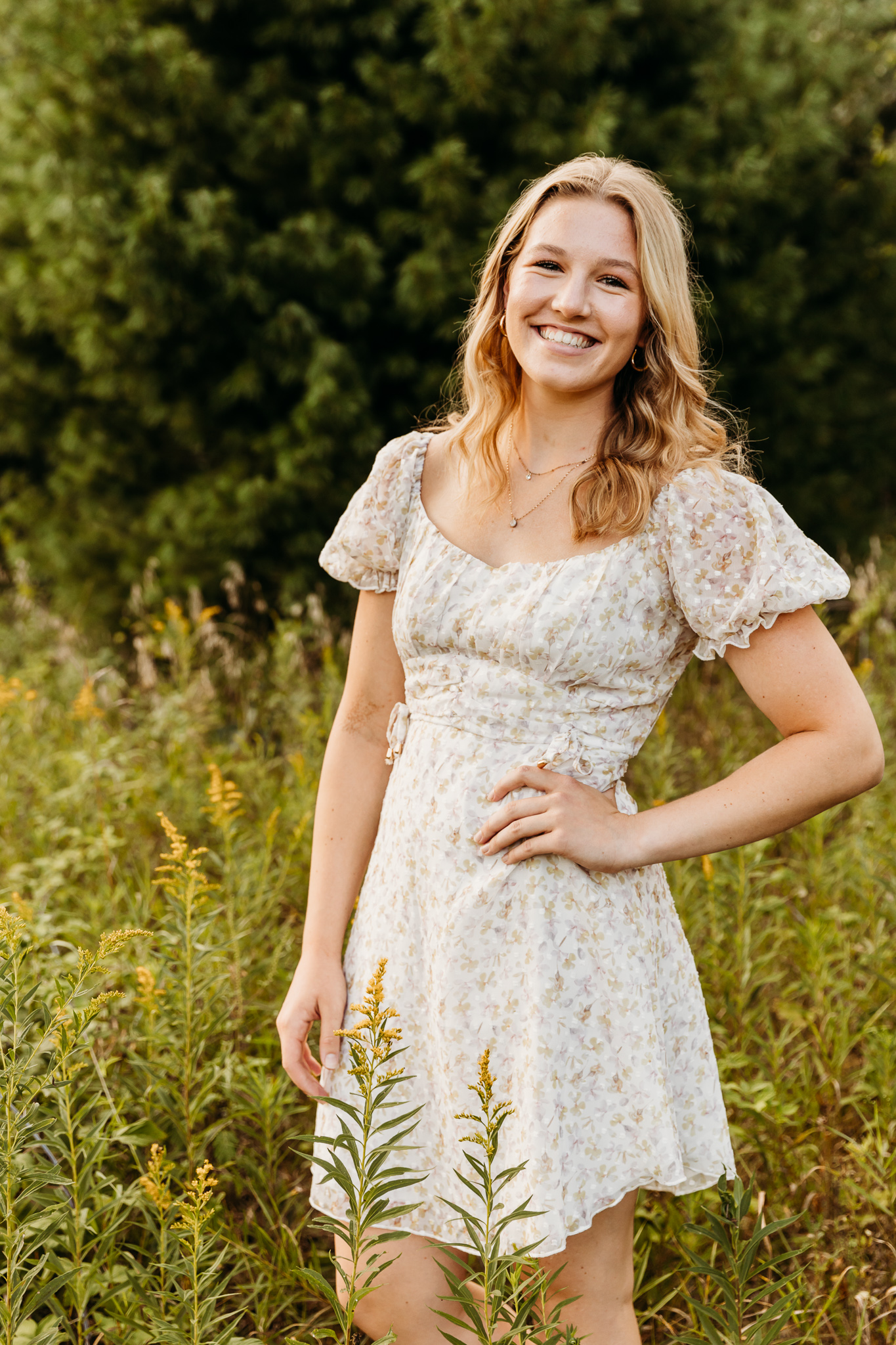 high school senior in a white dress posing in a field of goldenrod at sunset