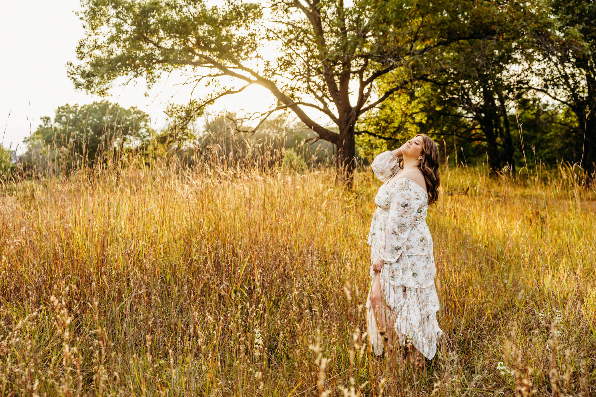 Gorgeous teen girl in a white dress playing with her hair as the sun sets behind her.