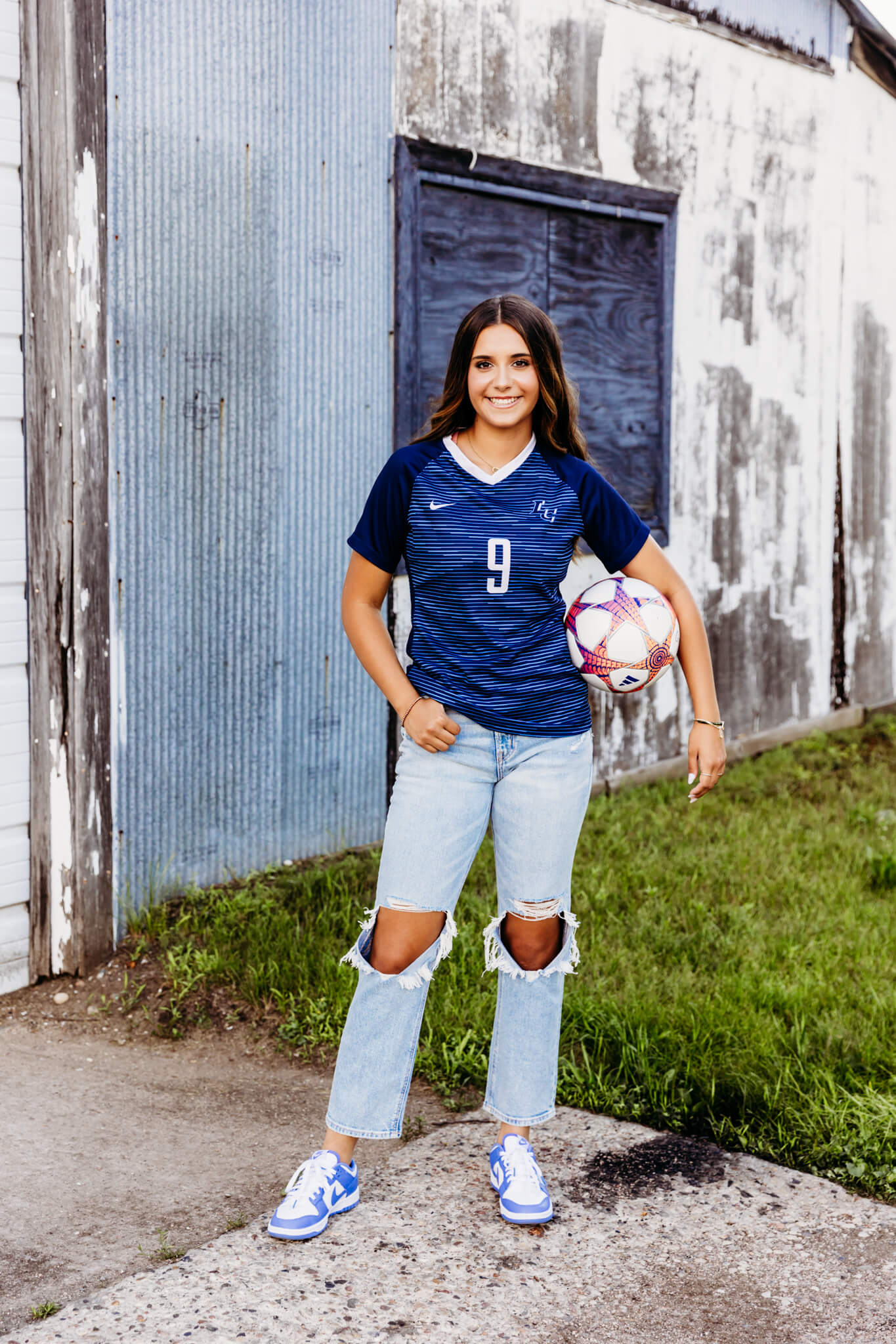 teenage girl in a soccer jersey from Kimberly High School holding her soccer ball in front of a building