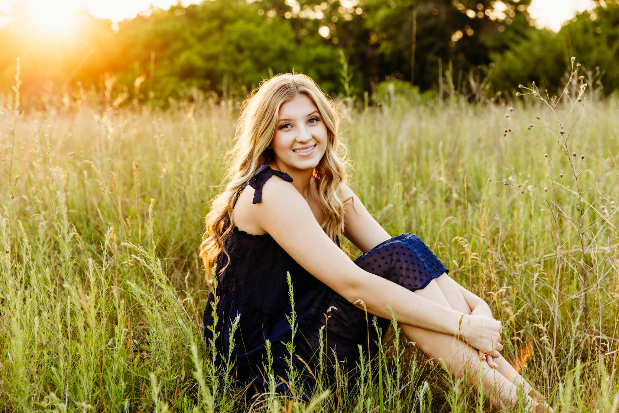 stunning high school girl sitting in the grass at sunset and smiling