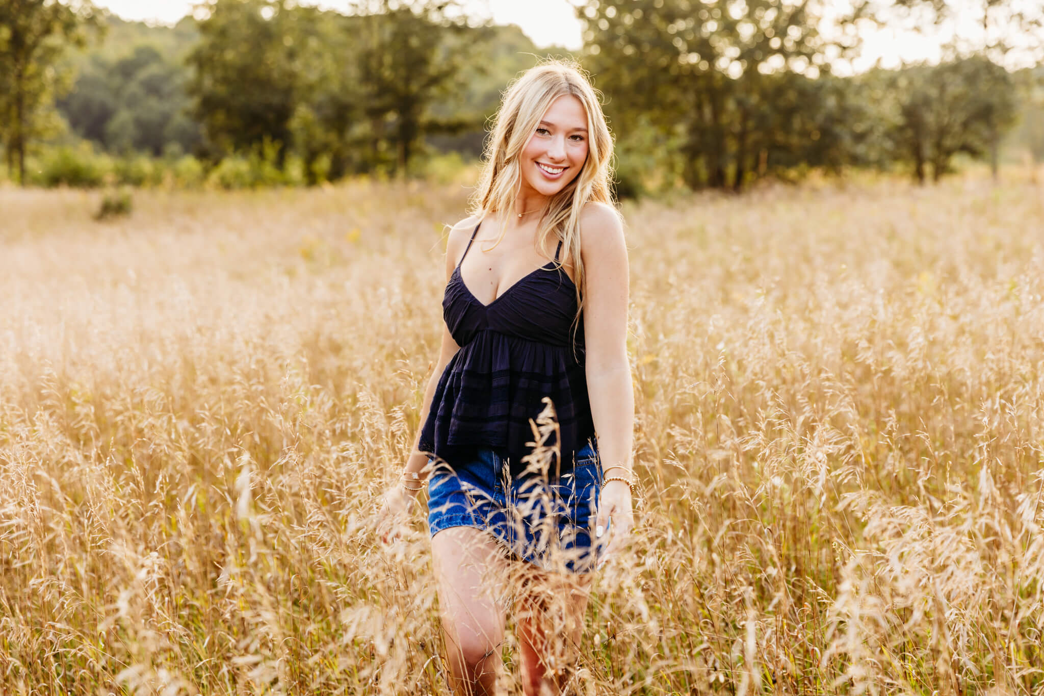 blonde teenage girl in a blue tank top and skirt walking through tall brown grass