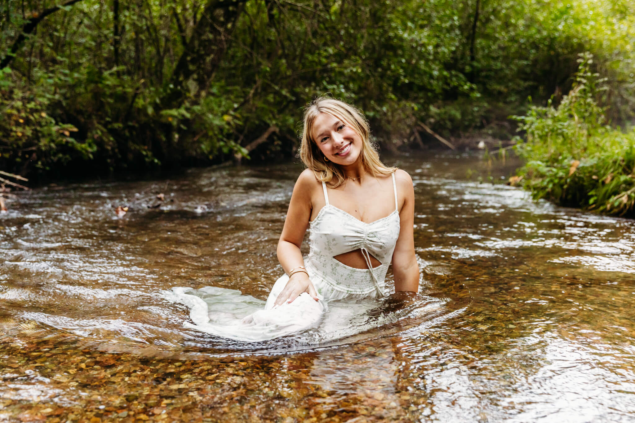 beautiful teen girl in a white dress sitting in a river and smiling