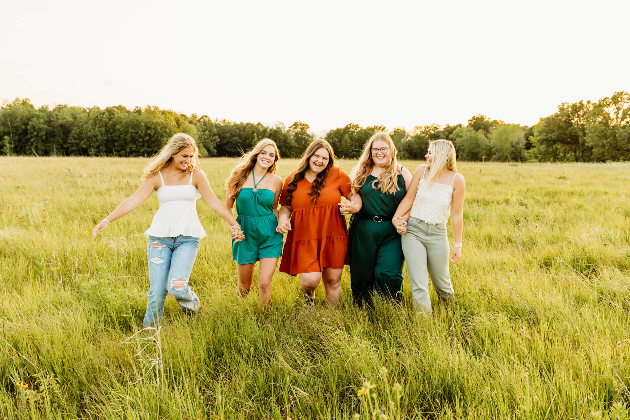 group of teenage girls laughing together as they walk through a grassy field