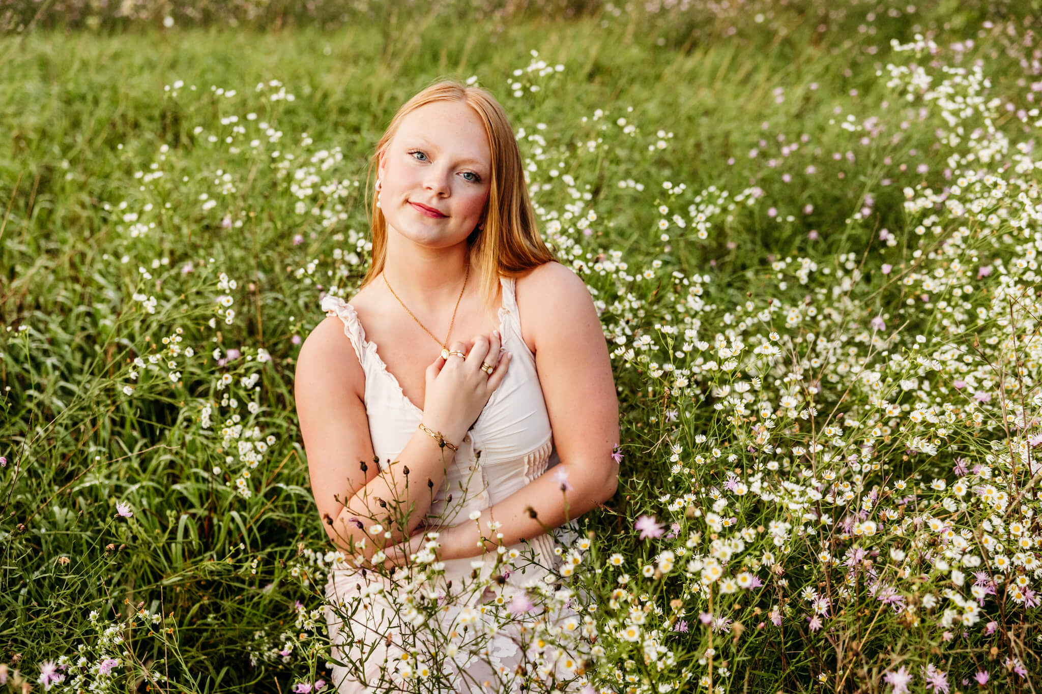 Beautiful teenage girl sitting in a field and surrounded by tons of wildflowers.