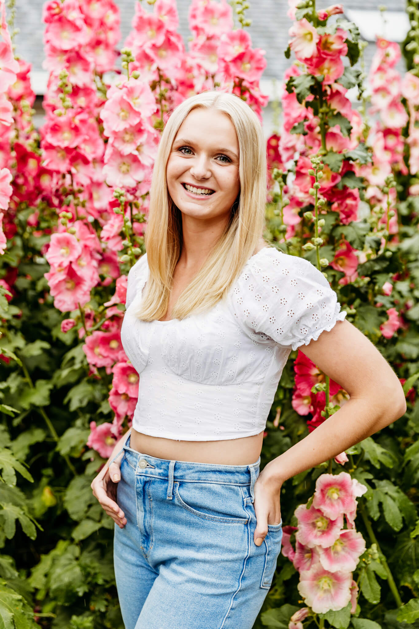 beautiful blonde teen girl in a white crop top and jeans standing in front of pink flowers for blog post about Fred and Co Fish Creek