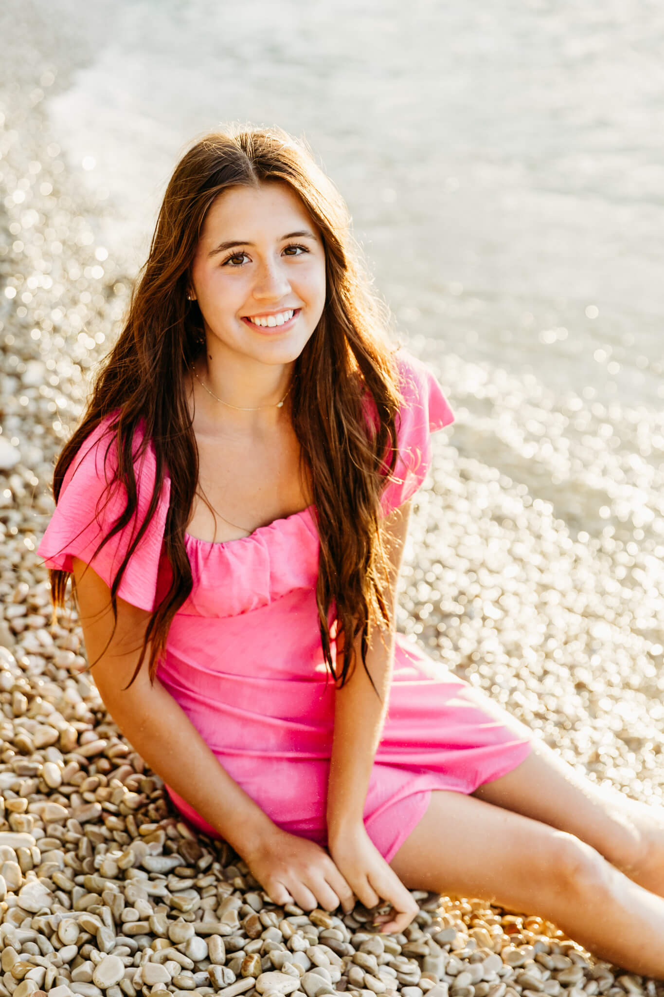 teen girl in a bright pink dress sitting on a white pebble beach in Door County for a blog post about Blue Ivy in Fish Creek