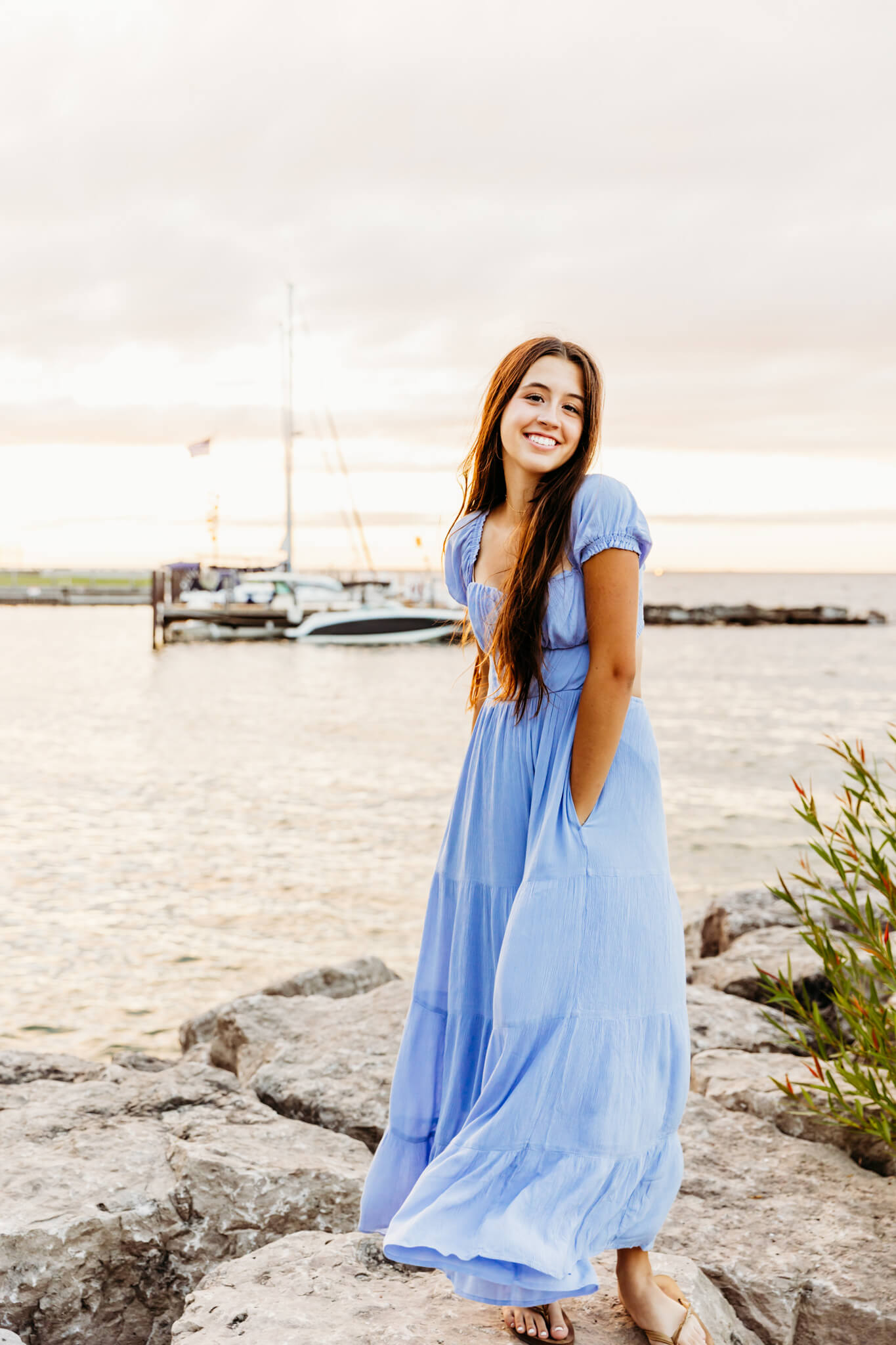 high school teen twirling in her long blue dress while standing on a rocky shore in Door County
