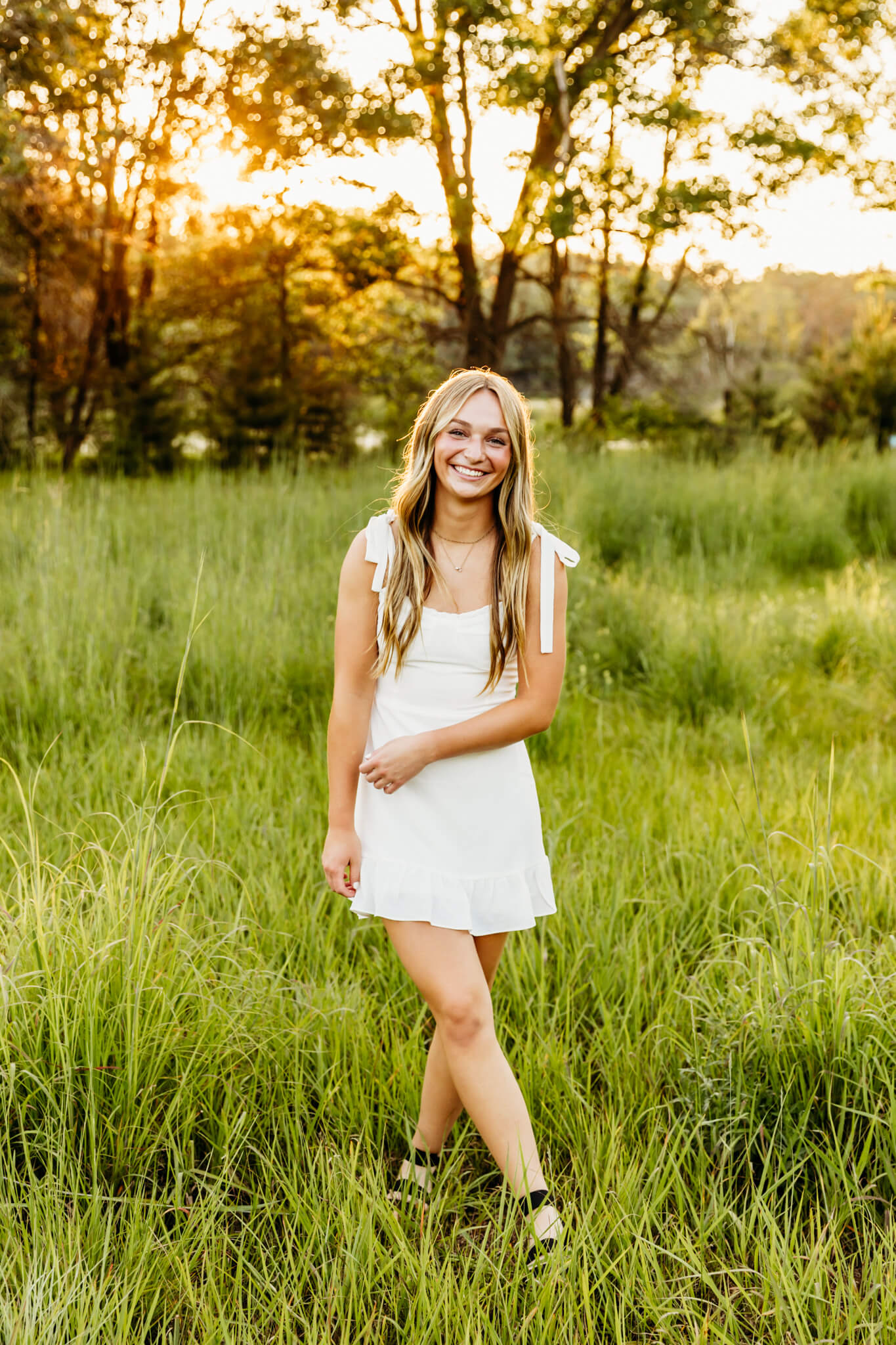 gorgeous teen in a short white dress, laughing as she walks in tall grass for a blog post about tanning in Green Bay WI
