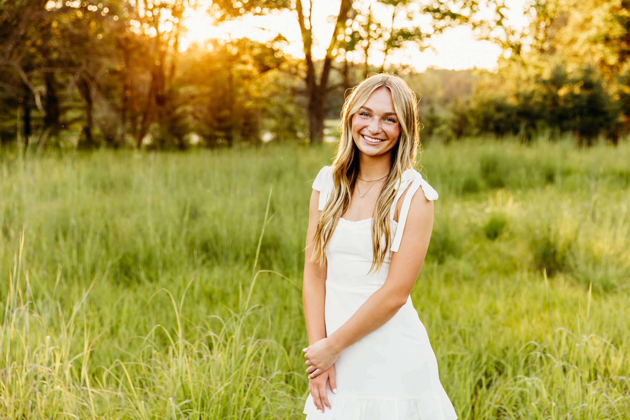stunning teen girl in a white dress standing in a glowing field at sunset near Green Bay