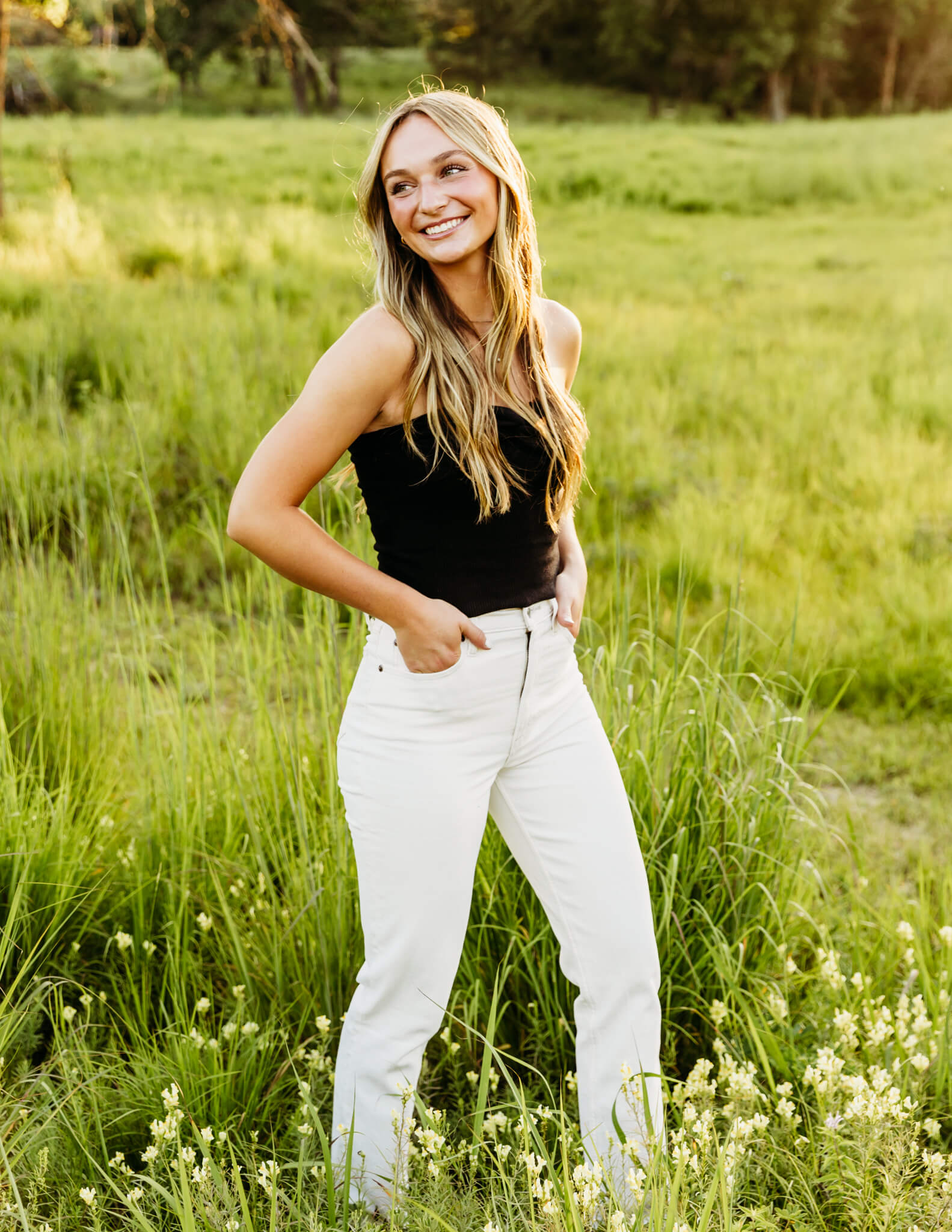 beautiful teen girl in black top and white pants walking the wildflowers as she looks over her shoulder and laughs