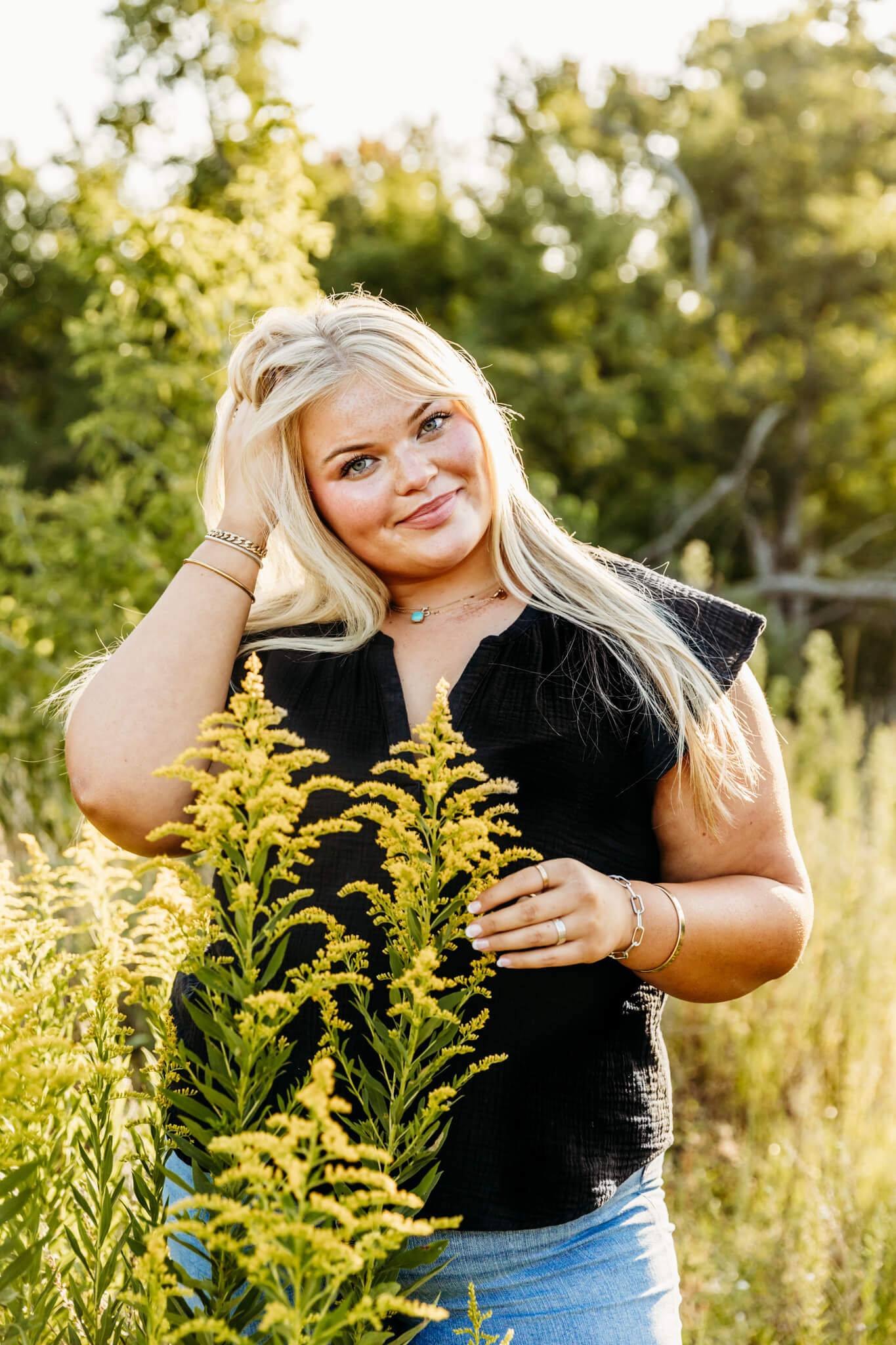 gorgeous blonde teen girl in a black top and jeans playing with her hair and she holds wildflowers