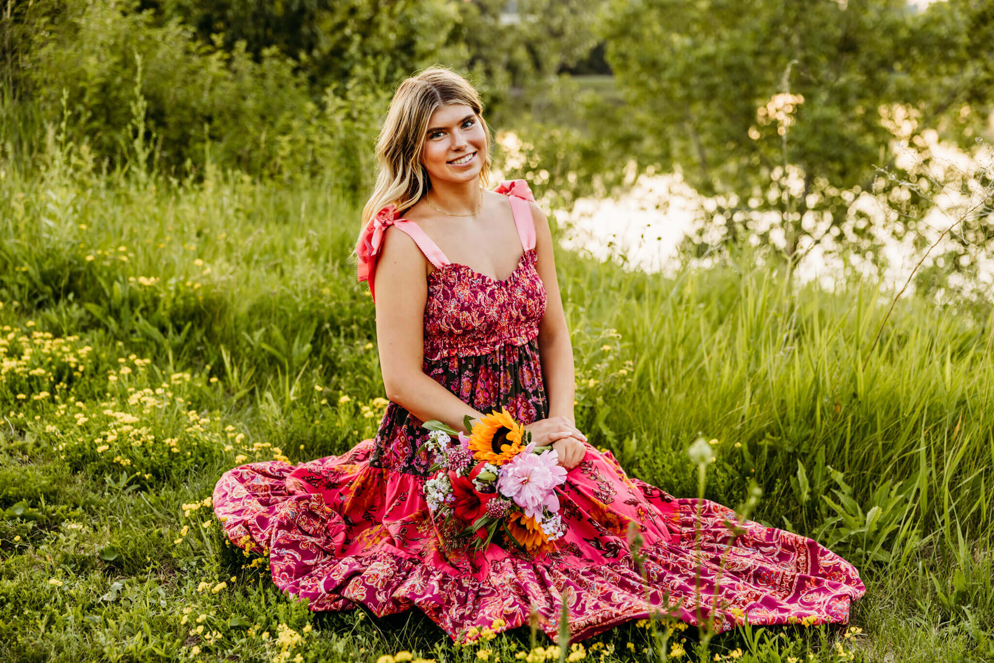 Oshkosh West high school senior girl in a pink dress sitting in the grass at sunset while holding a bouquet.