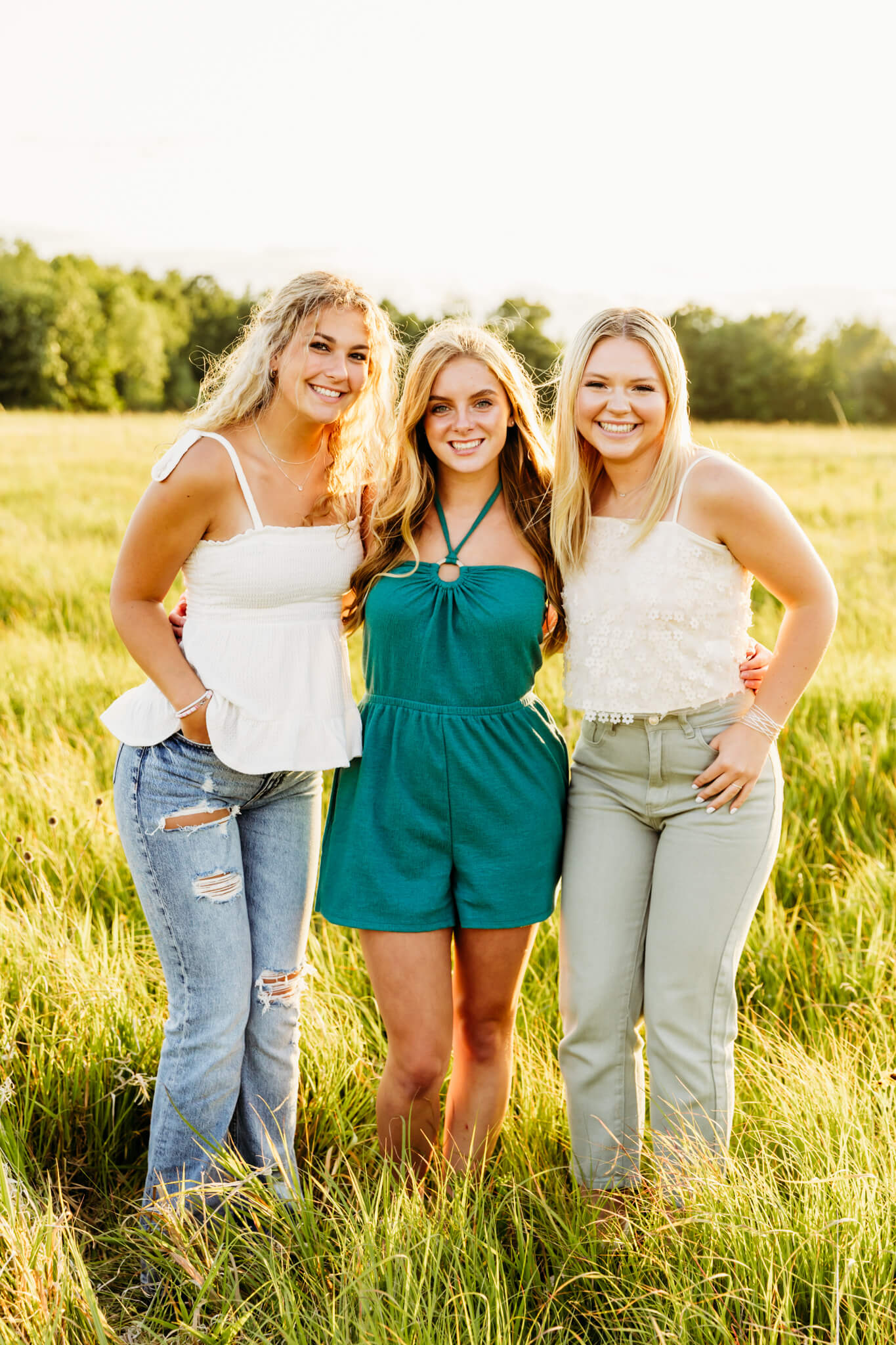 three teens smiling and hugging each other in a grassy field at sunset