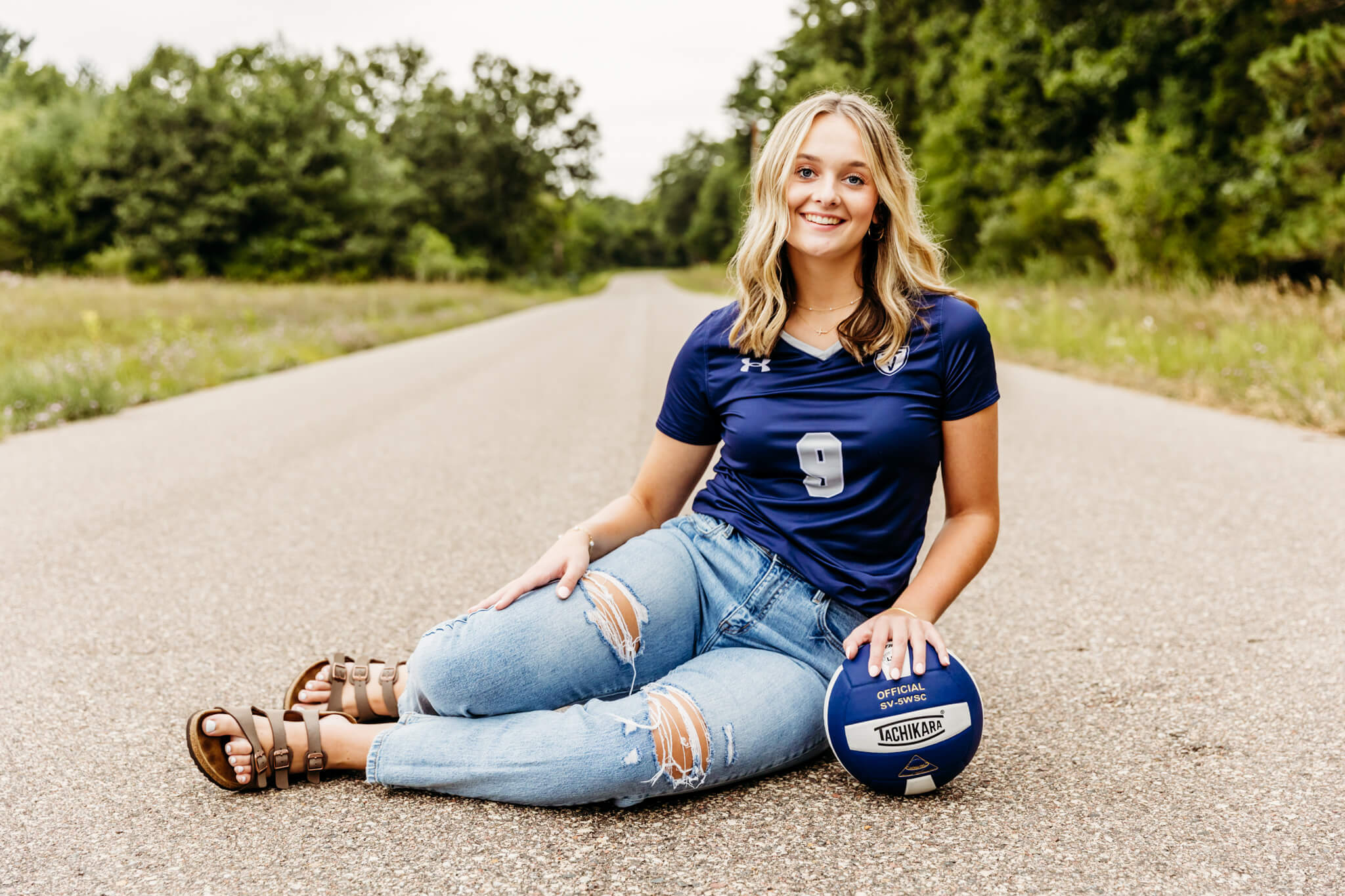 high school girl in her volleyball uniform sitting on a backroad and leaning against a volleyball for a blog post about Fox Cities Elite Volleyball