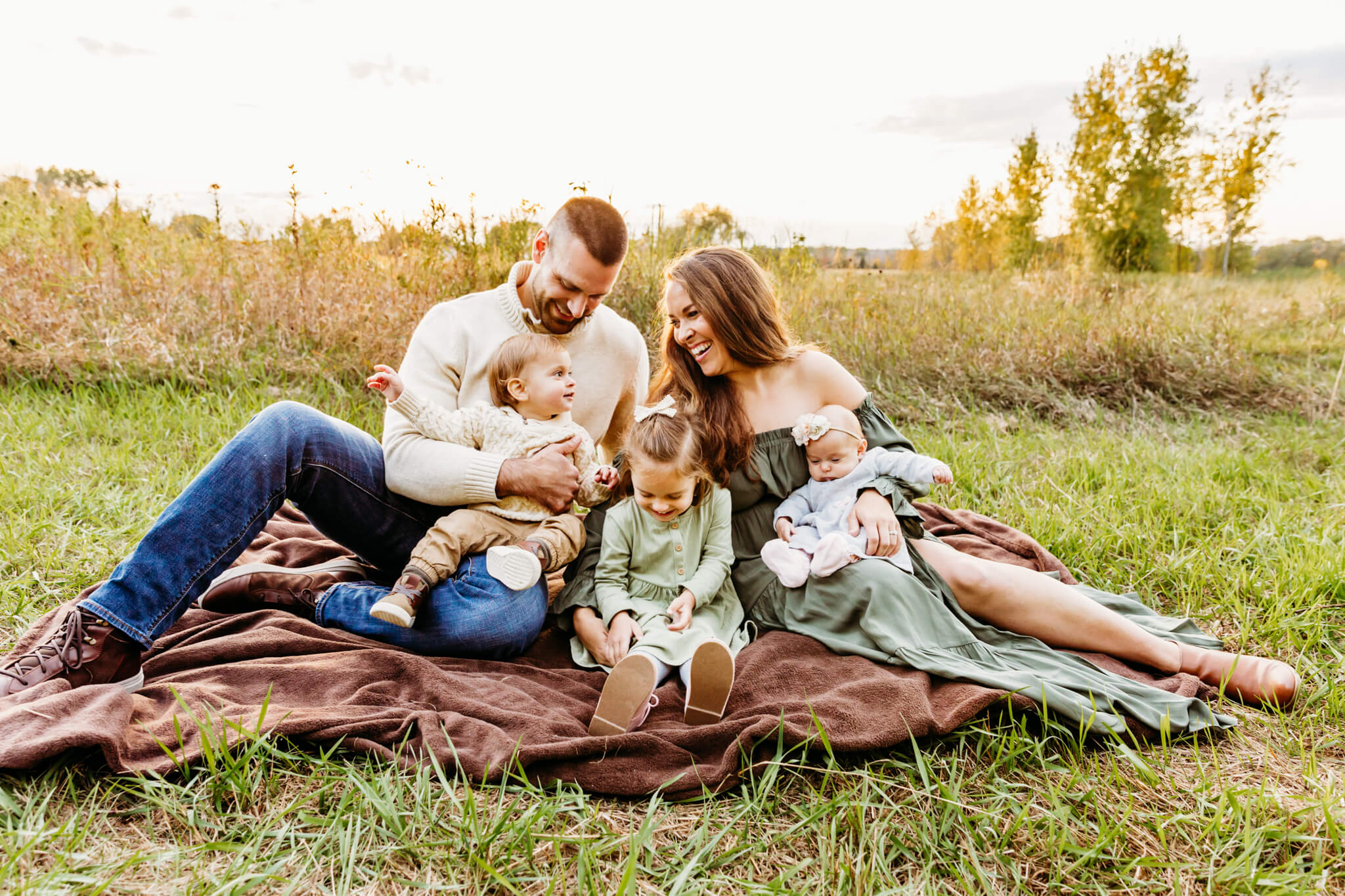 family of 5 sitting on a blanket in a beautiful green field in the fall for blog post about Julie's Touch of Silver Dance Studio in Oshkosh