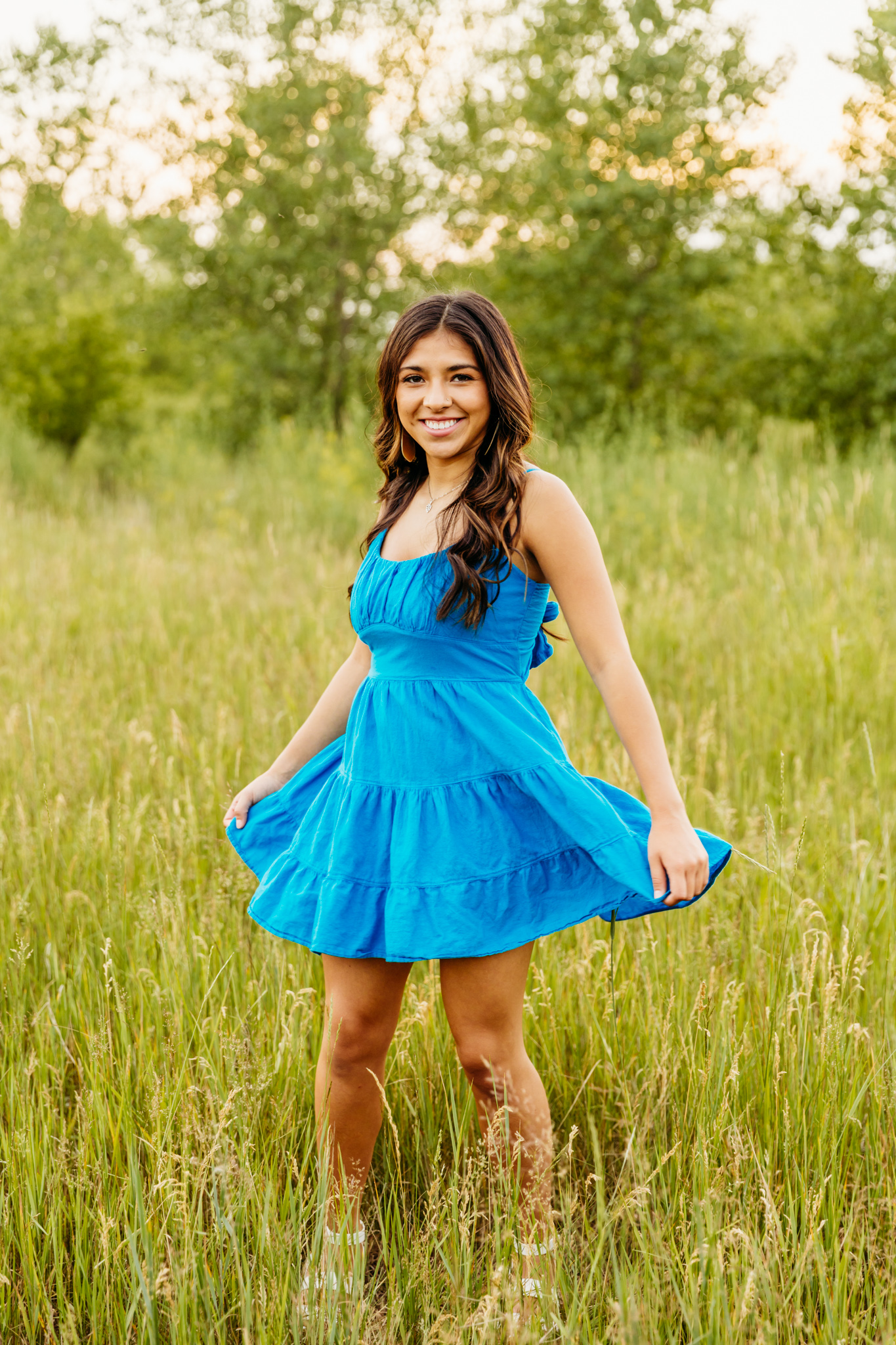 image of a beautiful teen girl in a bright blue dress wearing her brown curly hair down, as she twirls in a grassy field near Winneconne