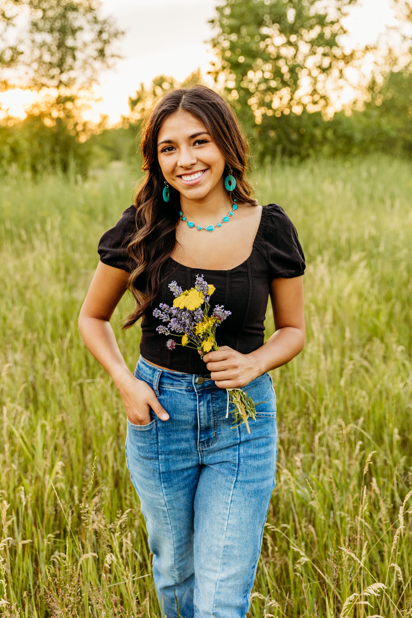 high school girl in a black top, denim pants and turquoise jewelry smiling with one hand in her pocket and the other holding a bouquet of wildflowers for a blog post about Red's Boutique in Winneconne