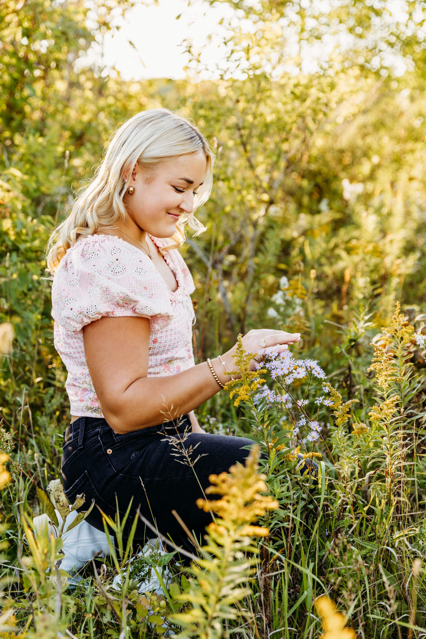 beautiful blonde high school senior kneeling next to flowers and playing with them as she smiles