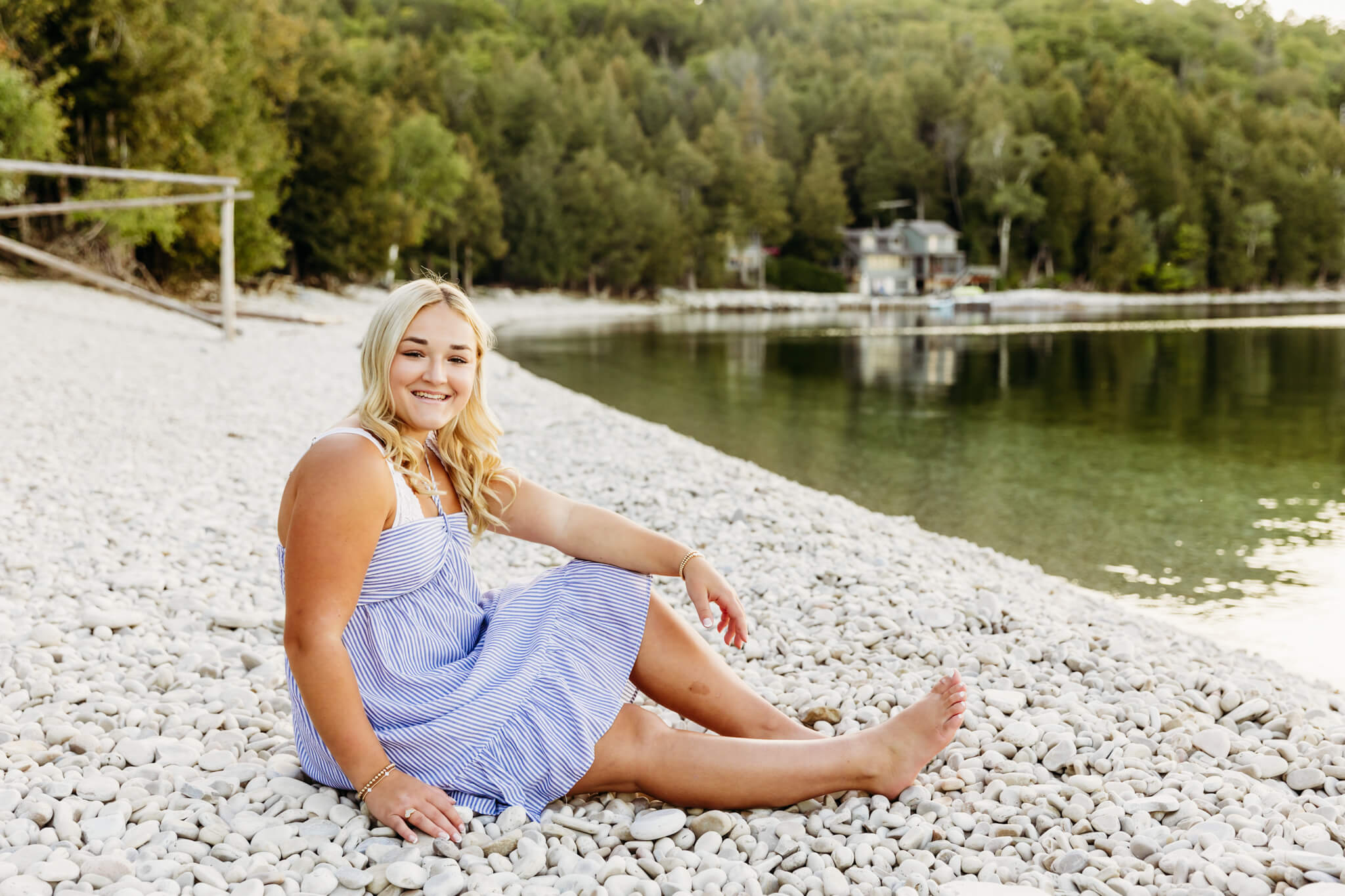 high school girl in a blue and white striped dress sitting on a rocky beach and smiling for a blog post about Spot Clothing in Door County