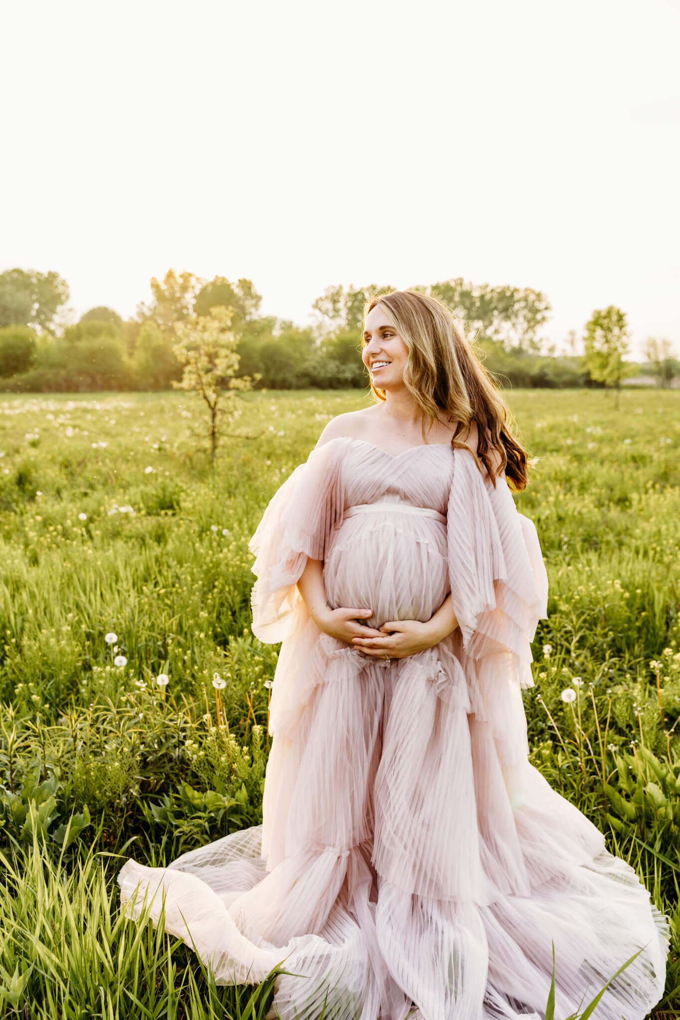 glowing mama to be holding her baby bump while standing in a field for post about Green Bay Doulas