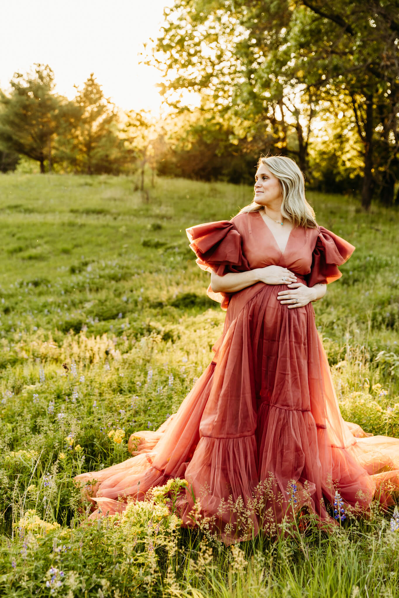 expecting mama in a beautiful maternity gown resting her hands on her baby bump as she looks into the field for a blog about Massages in Fond du Lac