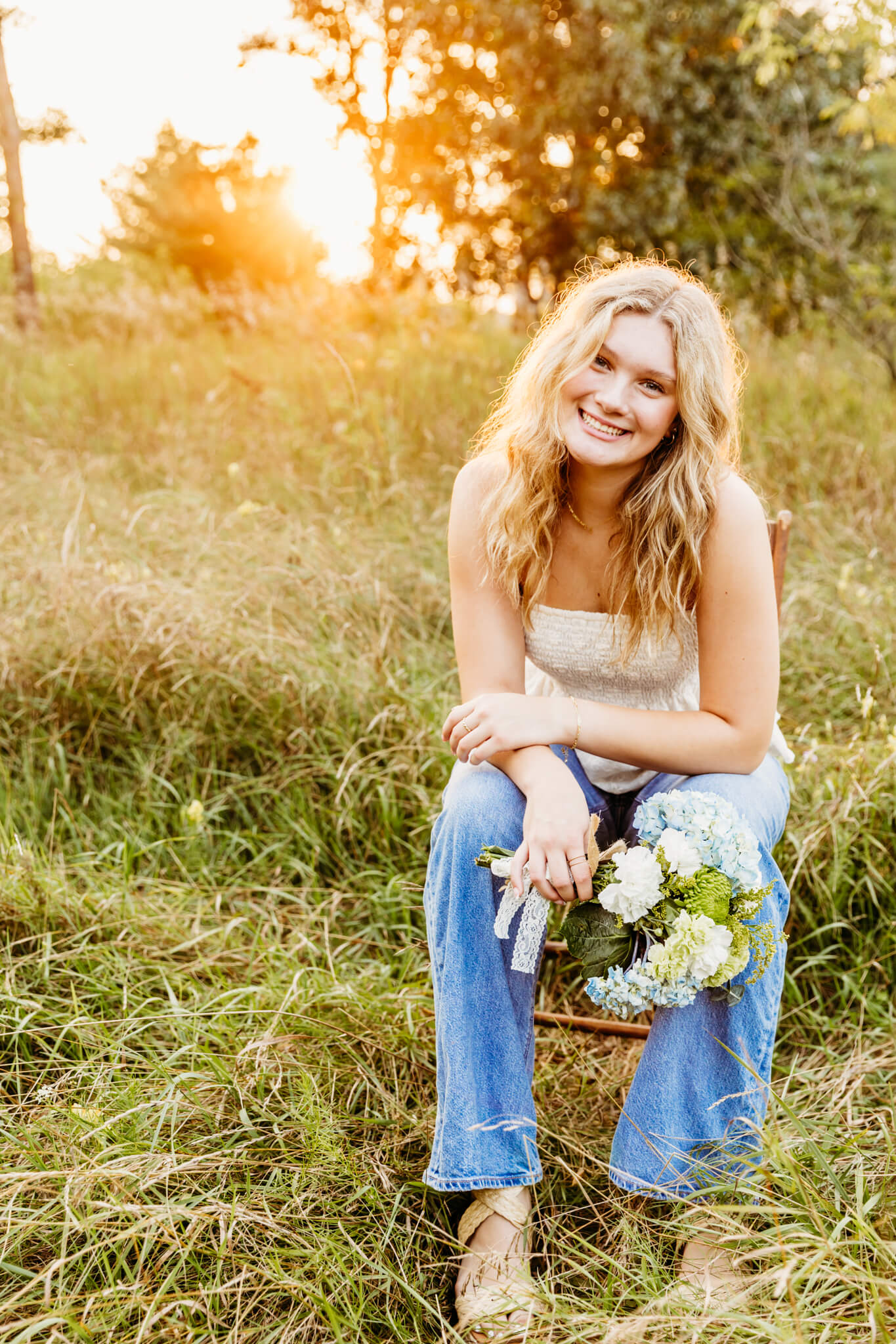 teen girl sitting on a chair in a field at sunset and holding a flower bouquet