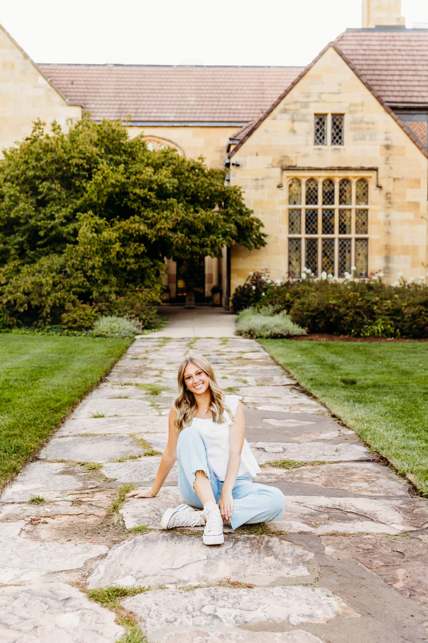 high school student sitting on a path in front of Paine Art Center for her senior photos