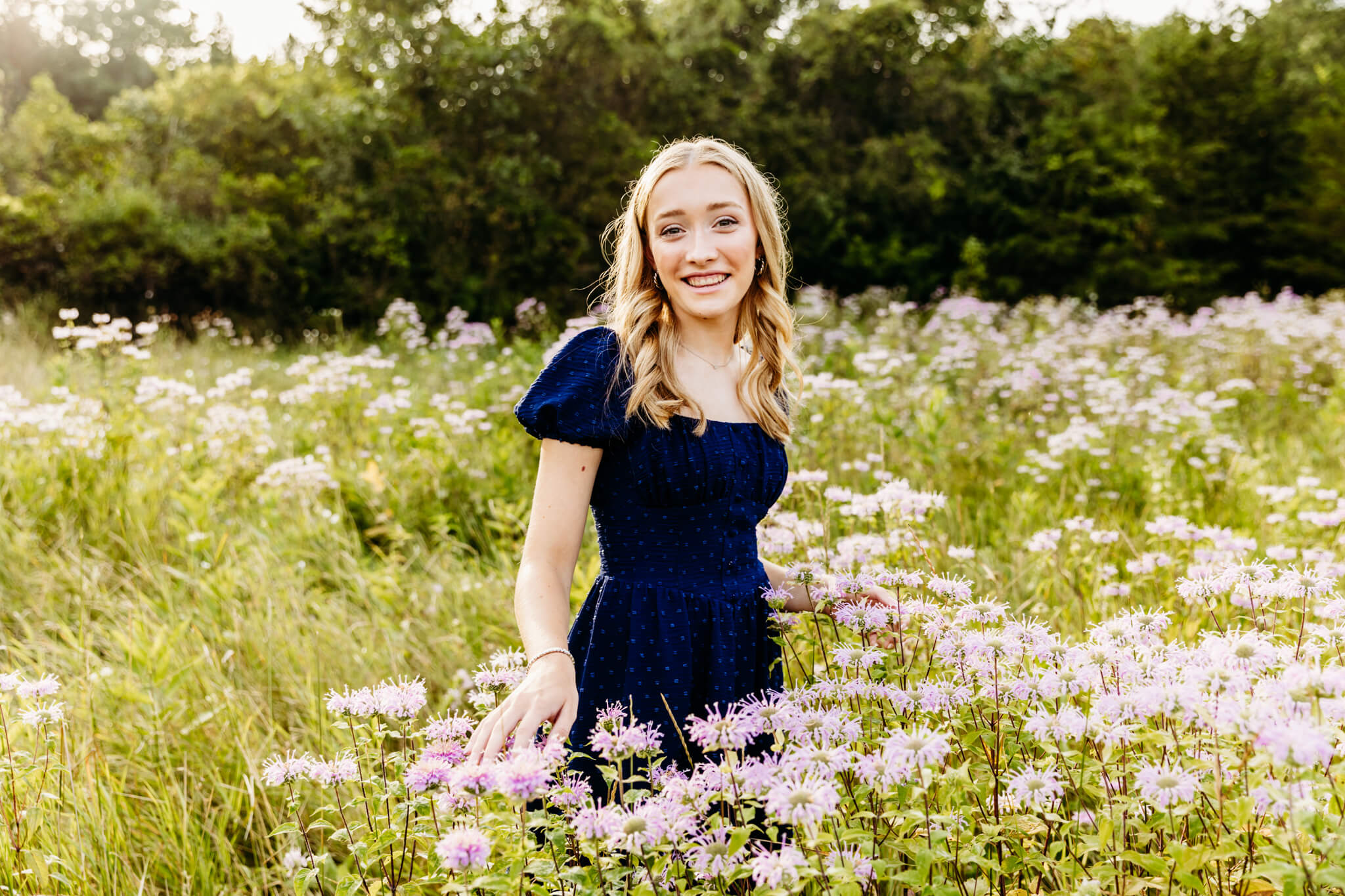 teen girl in a blue dress walking through purple wildflowers during her senior session