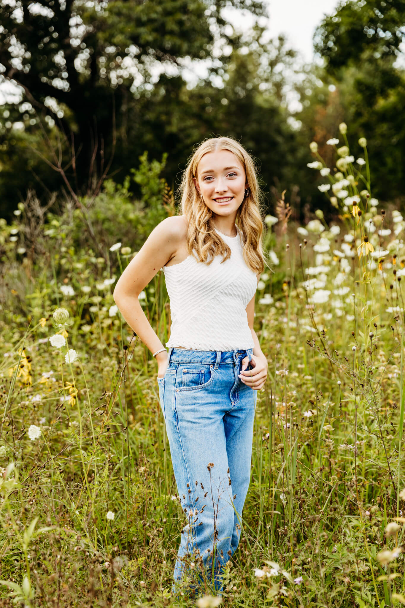 teenage girl in a white top and jeans standing in a flower field 