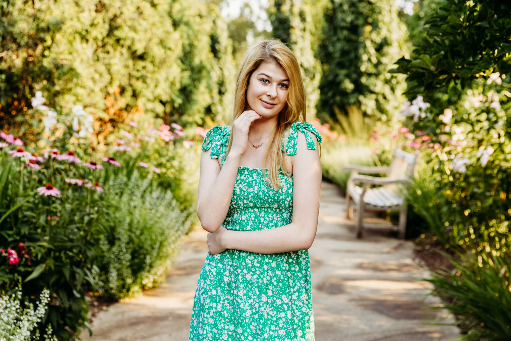 teenage girl in a green dress standing on a walkway between the flower gardens