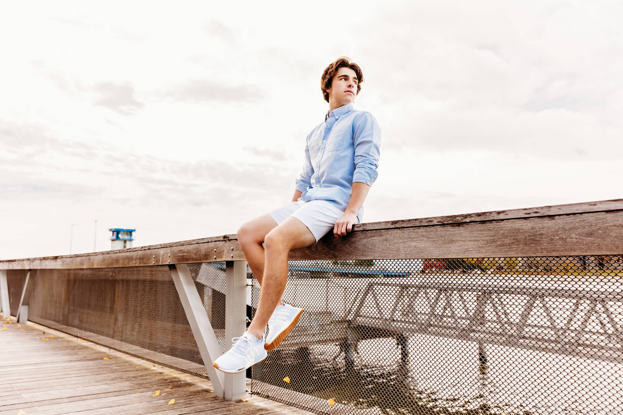 Senior boy sitting on the railing at the City Deck downtown Green Bay for his senior photography session.