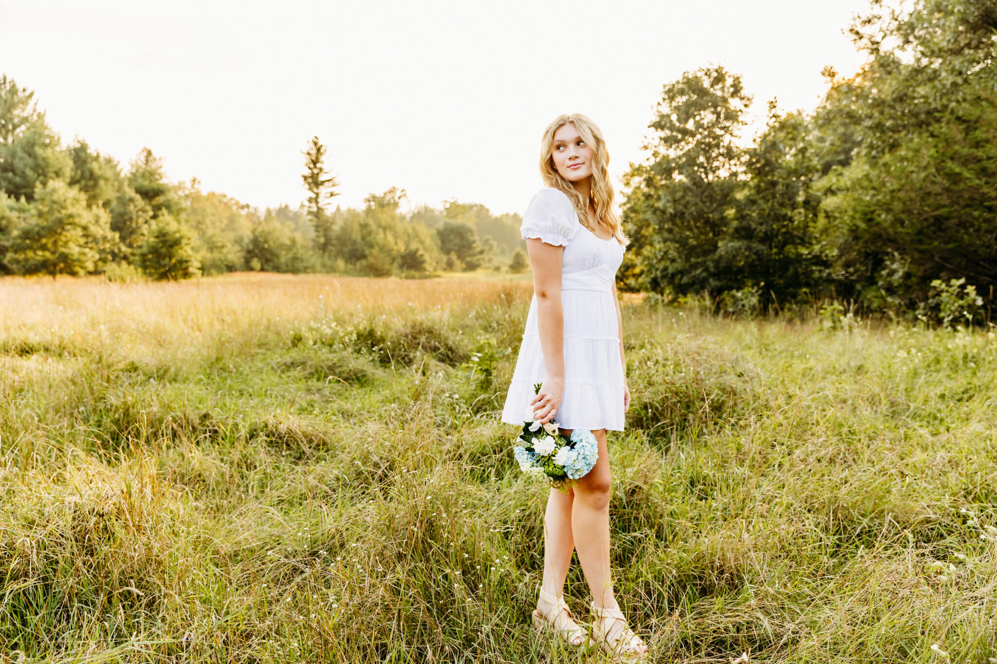 teen girl standing in a field at sunset and gazing out into the distance