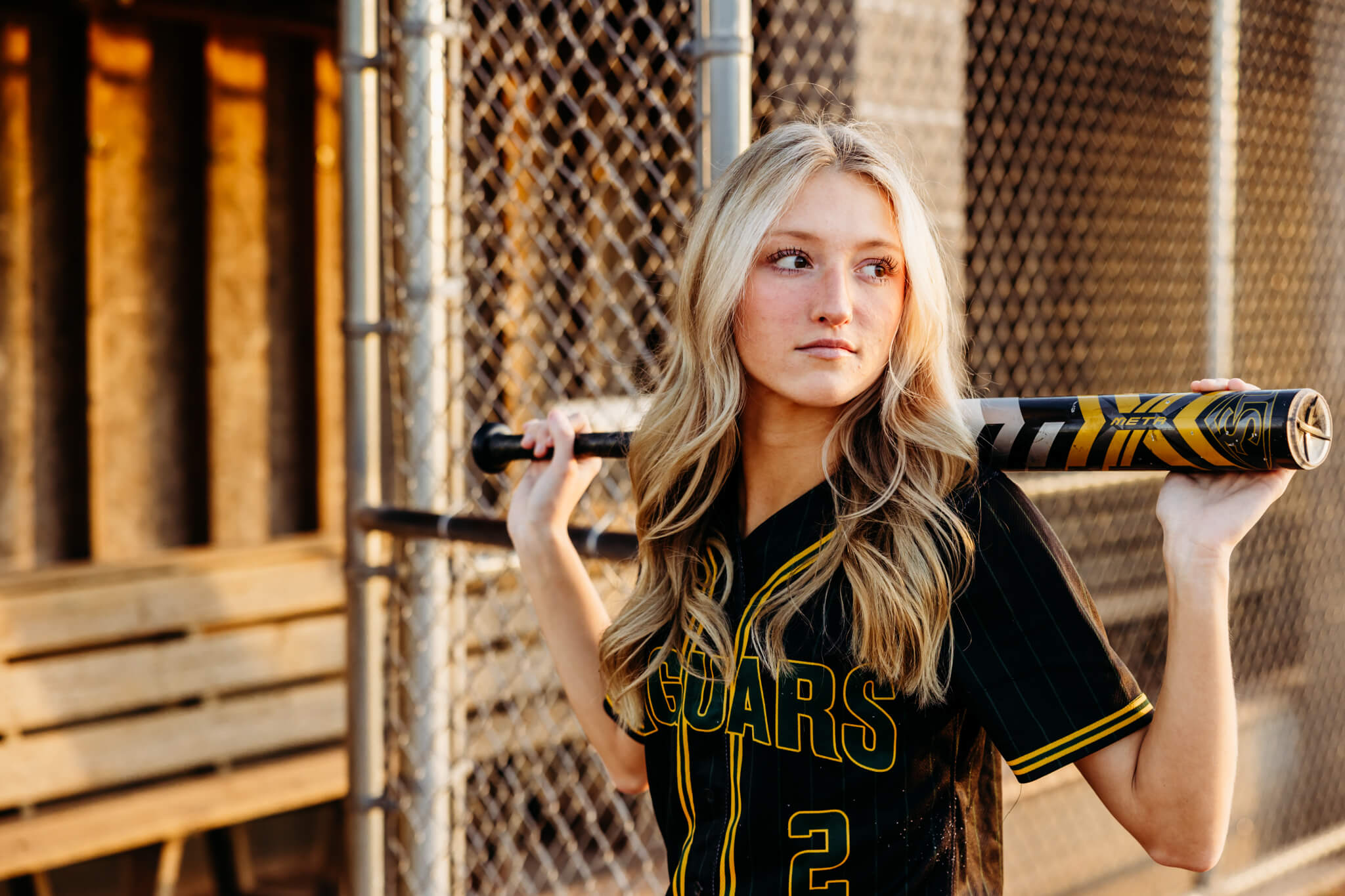 High school softball player resting a bat on her shoulders as she looks out into the softball field for a blog post about 360U Softball