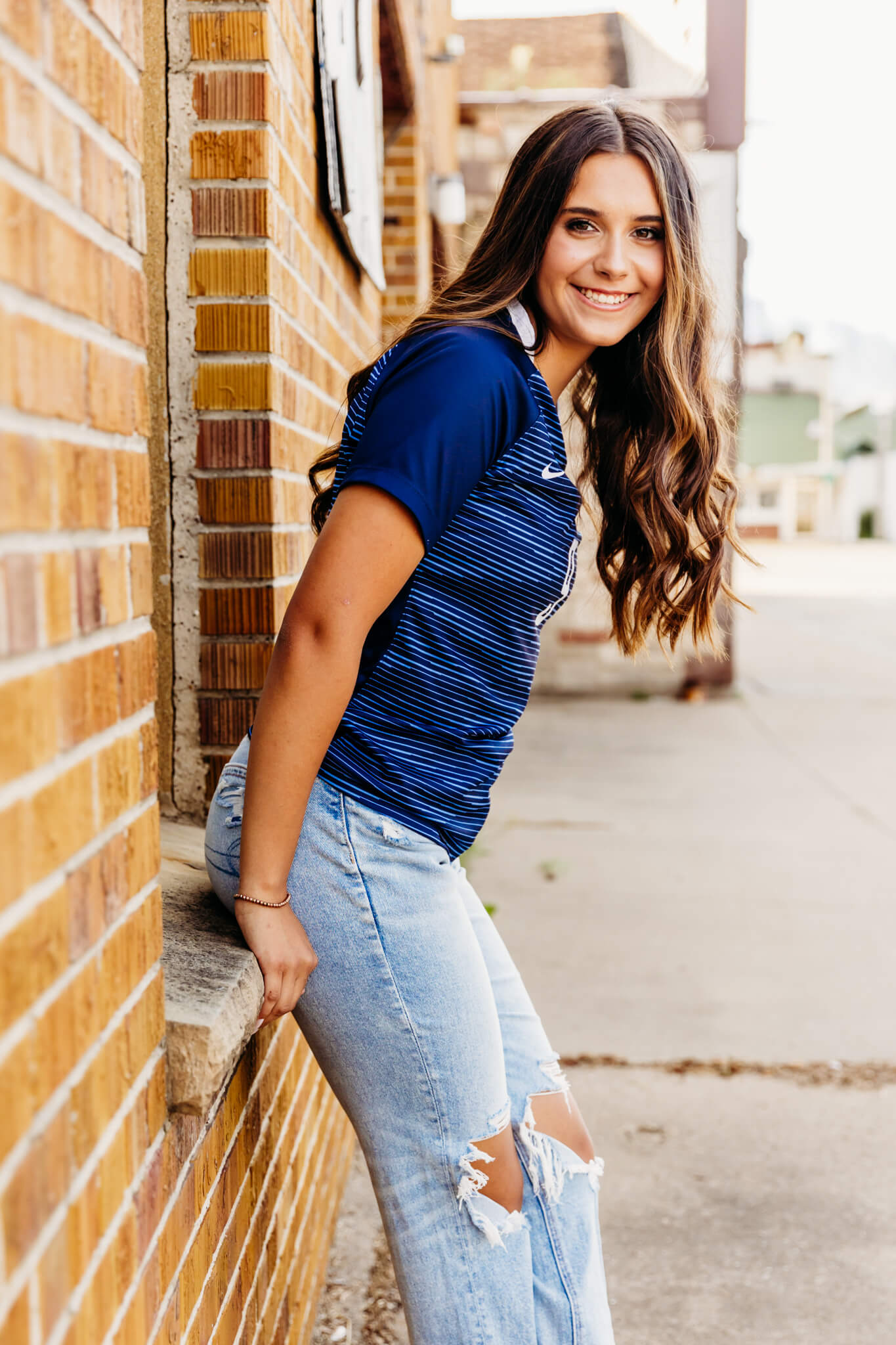 high school girl leaning against a brick window ledge and laughing as her hair falls in front of her